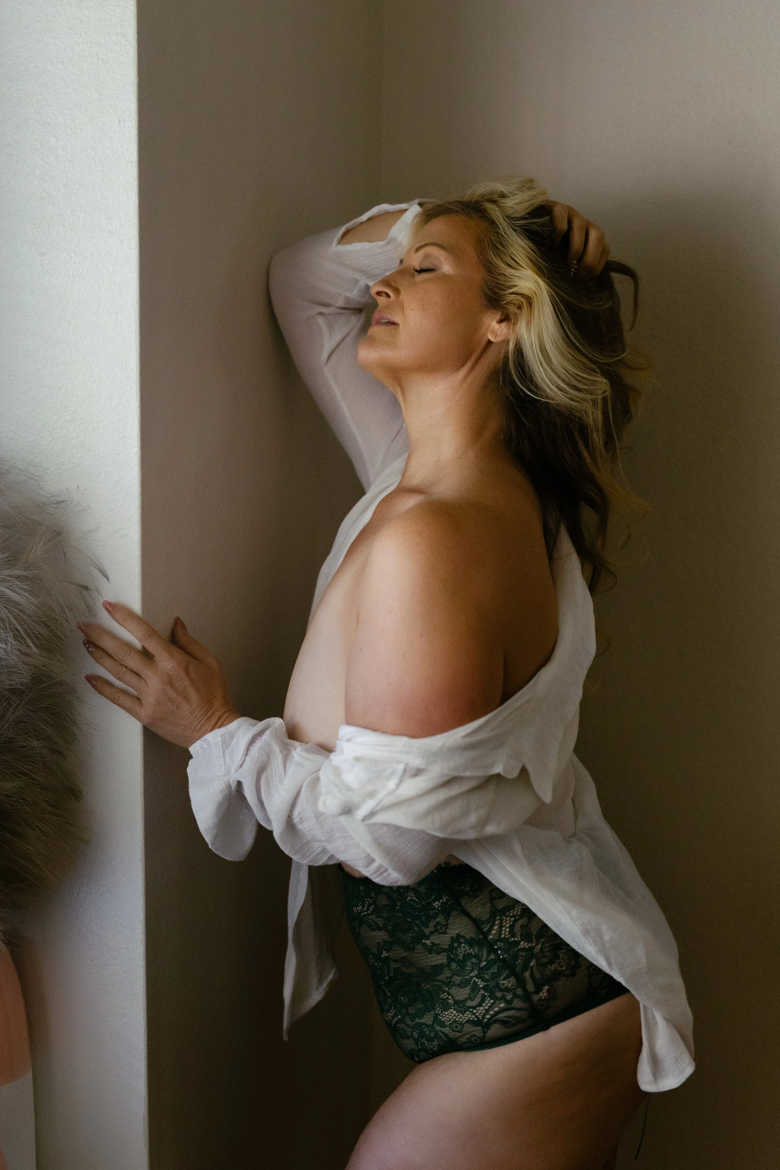 Boudoir photo of a client wearing a sheer white button down top, highlighting delicate lace details and subtle, flattering shadows.