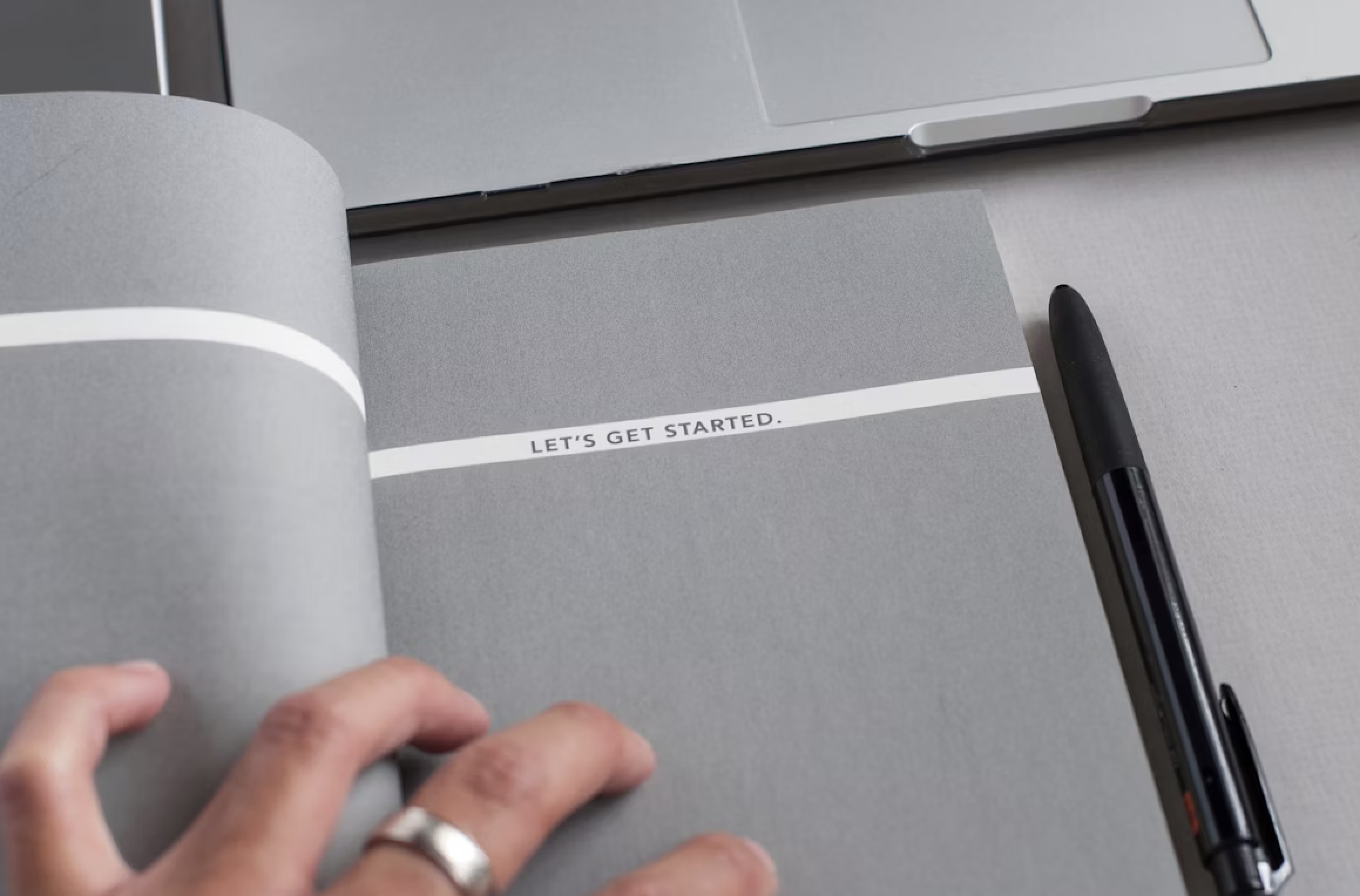 Notebook opened to the first page with the text "Let's get started." with a ben and laptop computer visible nearby.