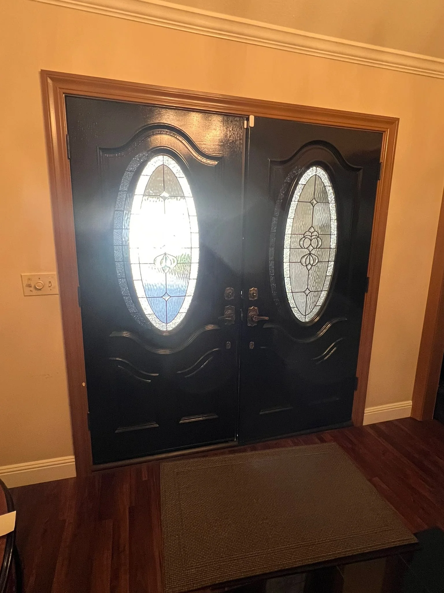 Double front door with decorative oval glass panels and wooden trim, with a doormat in front.