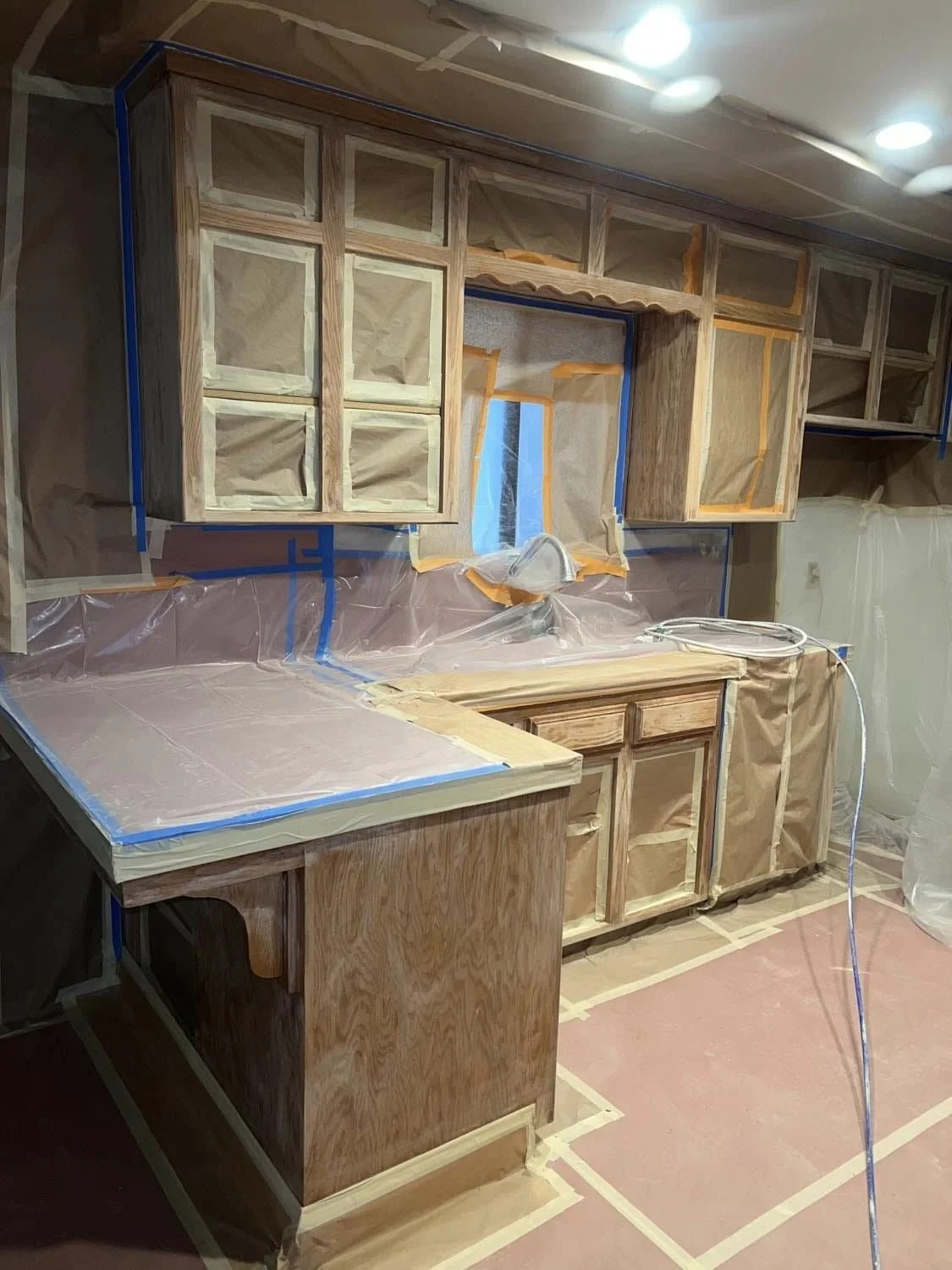 Kitchen cabinets under construction with some taped and covered areas, and plastic sheeting on the walls and counter.