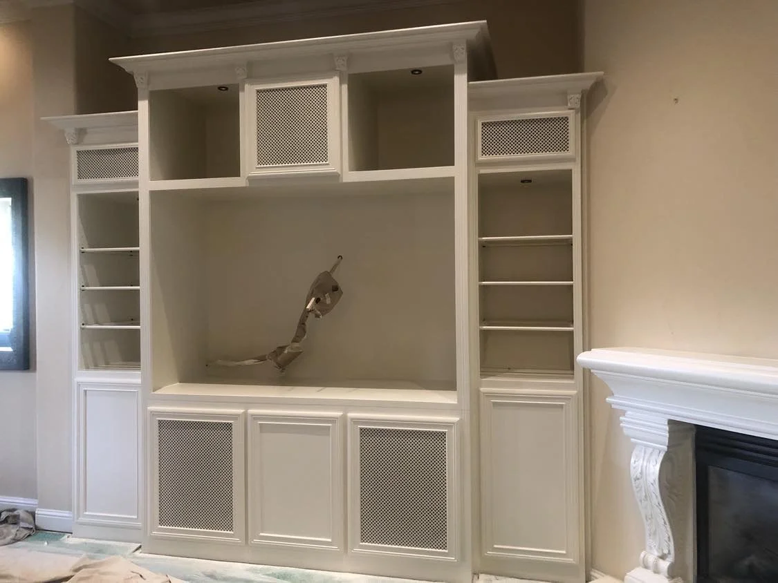 White built-in entertainment center with open shelves and cabinets, with a television mount in the center, next to a white fireplace with ornate molding.