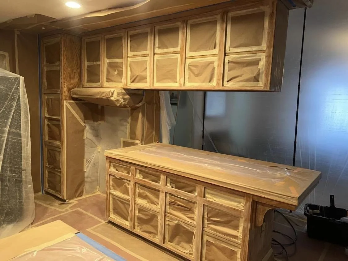 Unfinished wooden cabinets and countertop in a room under construction, covered with protective paper and tape.