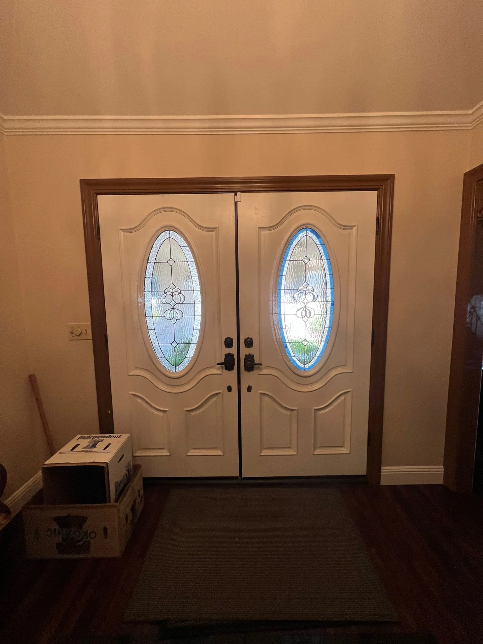 Double front door with decorative oval glass panels, beige walls, and hardwood flooring inside a house.