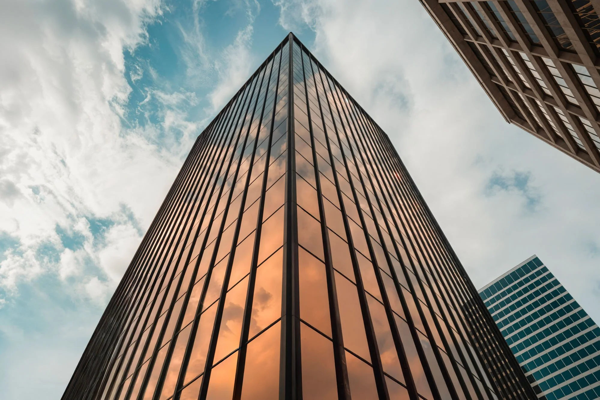 View of tall modern glass skyscraper reflecting the sky and clouds from a low angle.