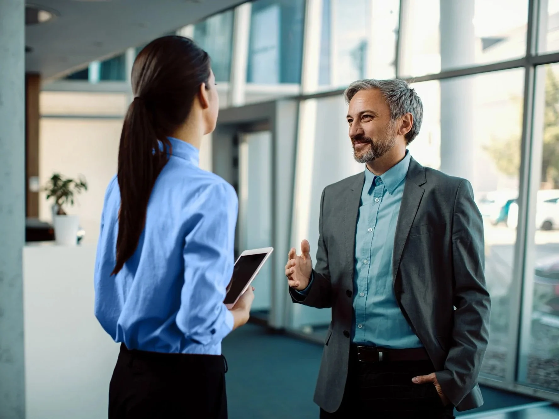 A man and a woman engaging in a conversation inside a modern office building with large glass windows.