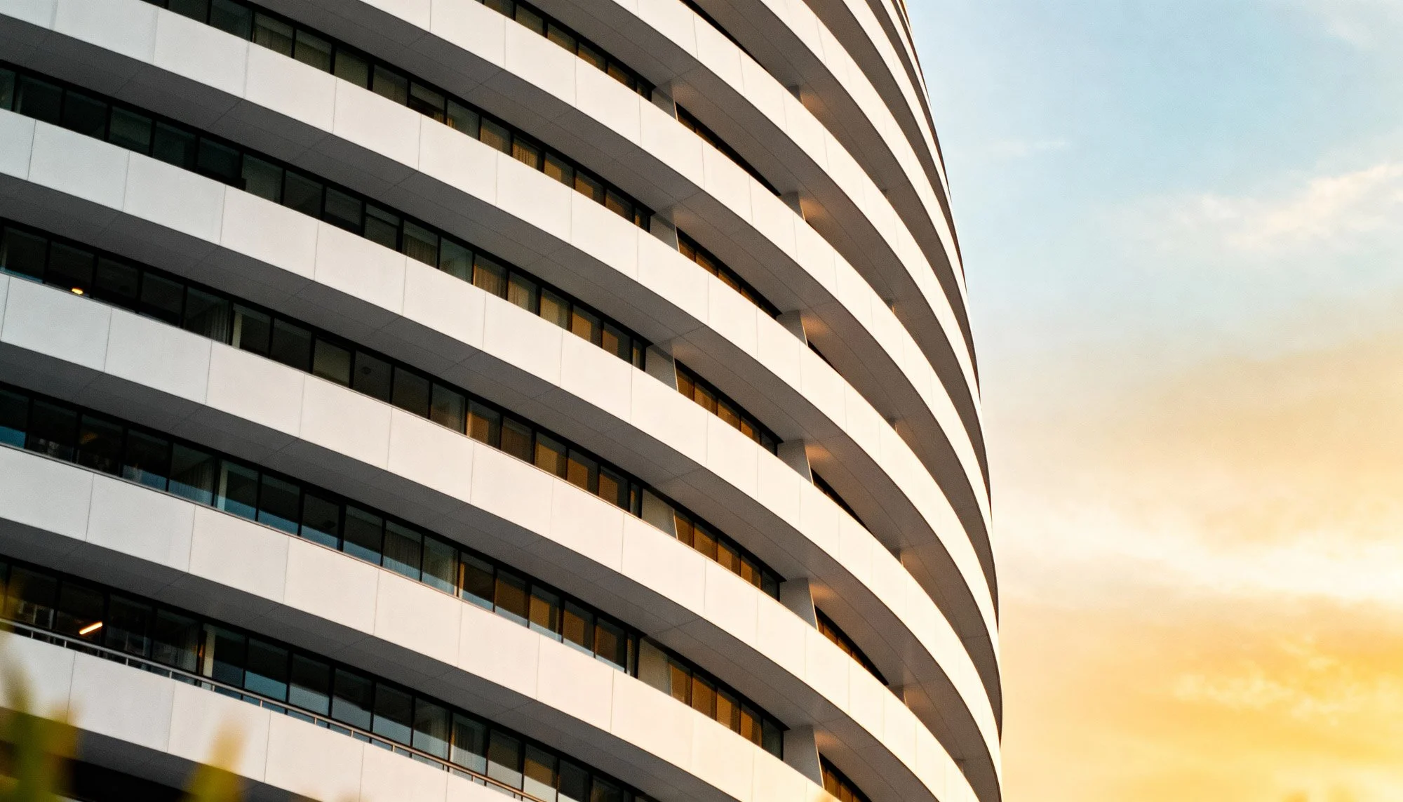 Modern high-rise building with curved lines and glass windows against a sunset sky.