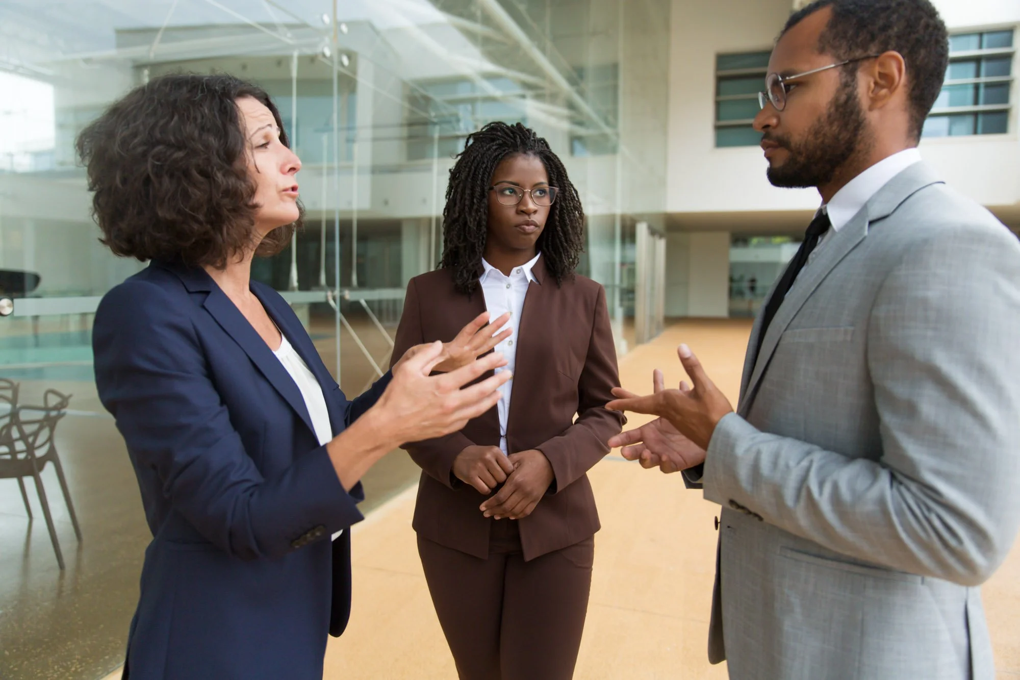 Three professionals having a serious conversation in a modern office building.