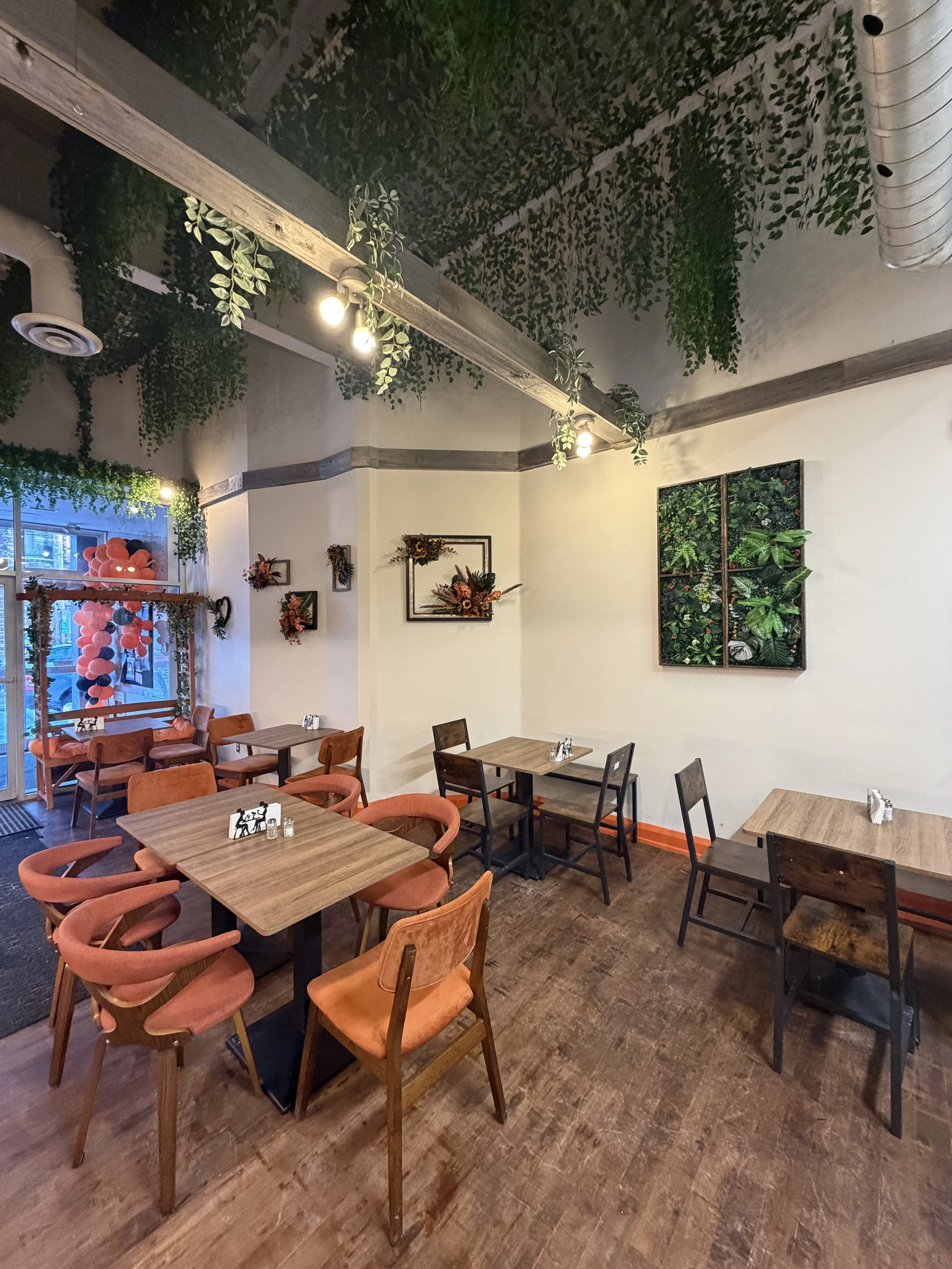 Interior of Solomon’s Oven in Ottawa featuring wooden tables, orange velvet chairs, hanging greenery, and a warm modern Levantine restaurant atmosphere.