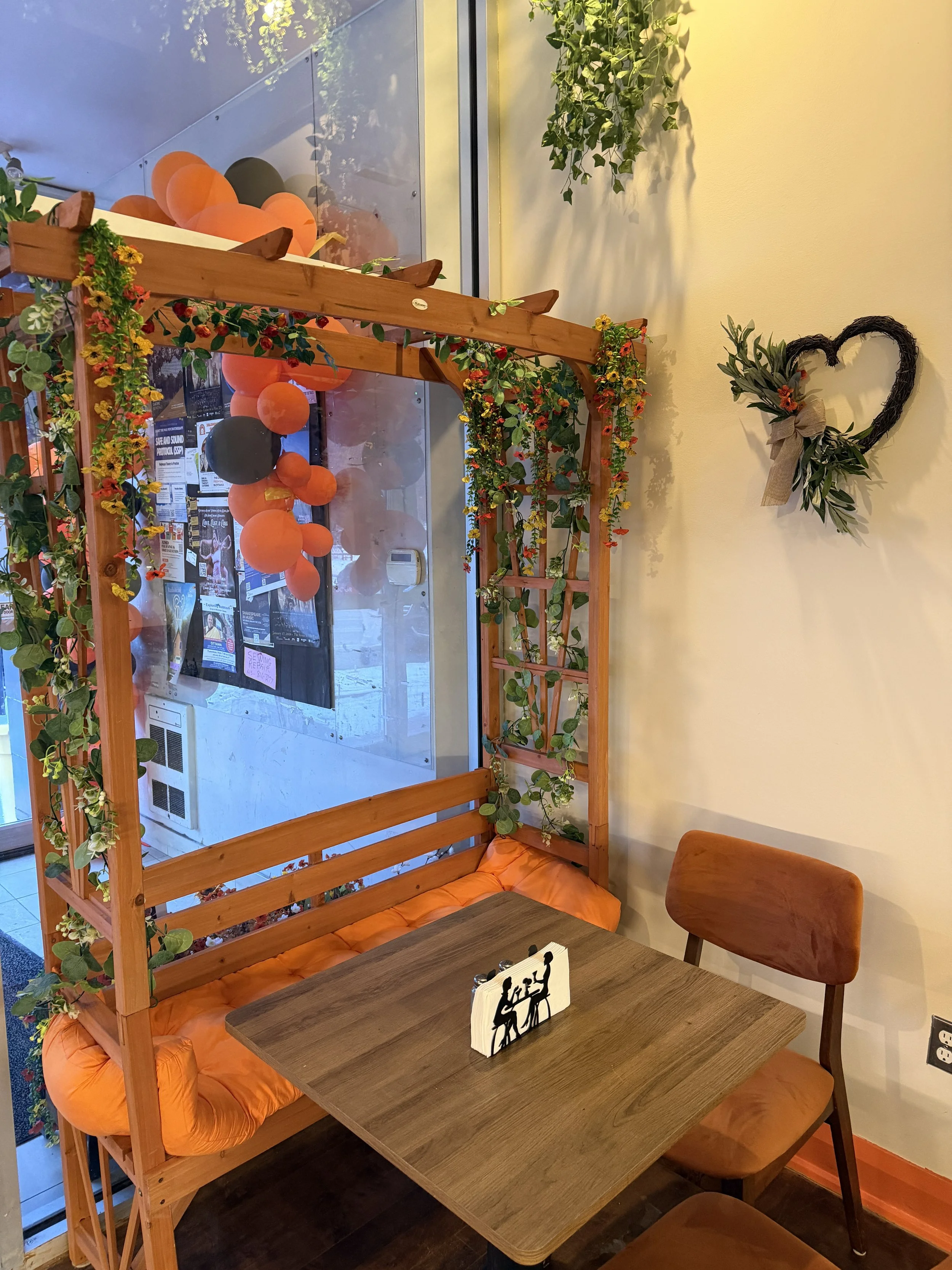 Cozy window seating with floral garland and orange accents at Solomon’s Oven Ottawa, a welcoming halal Levant kitchen near Wellington Street.