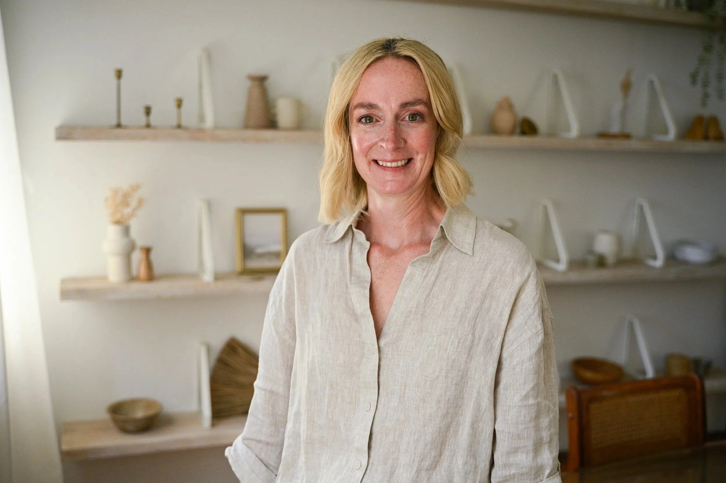 Dr. Sherry Purves smiling indoors, with shelves containing decorative vases, bowls, and picture frames in the background.