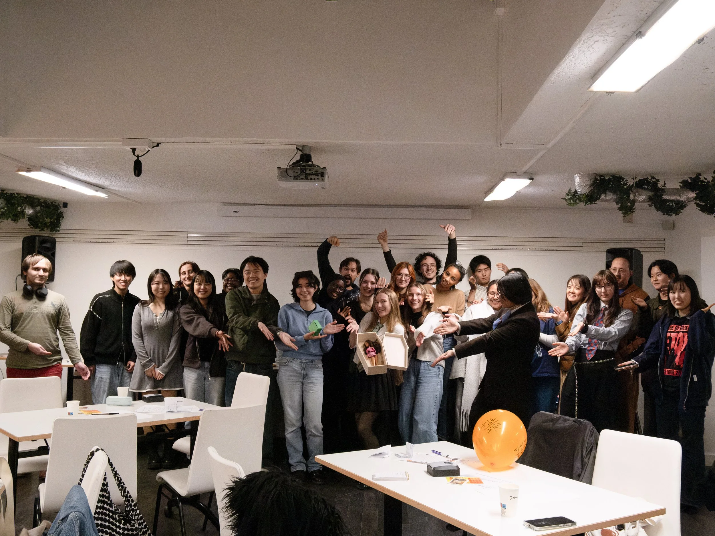 Groupe de personnes souriantes réunies dans une salle, participant à une célébration ou un événement, avec des décorations et un ballon orange sur une table.