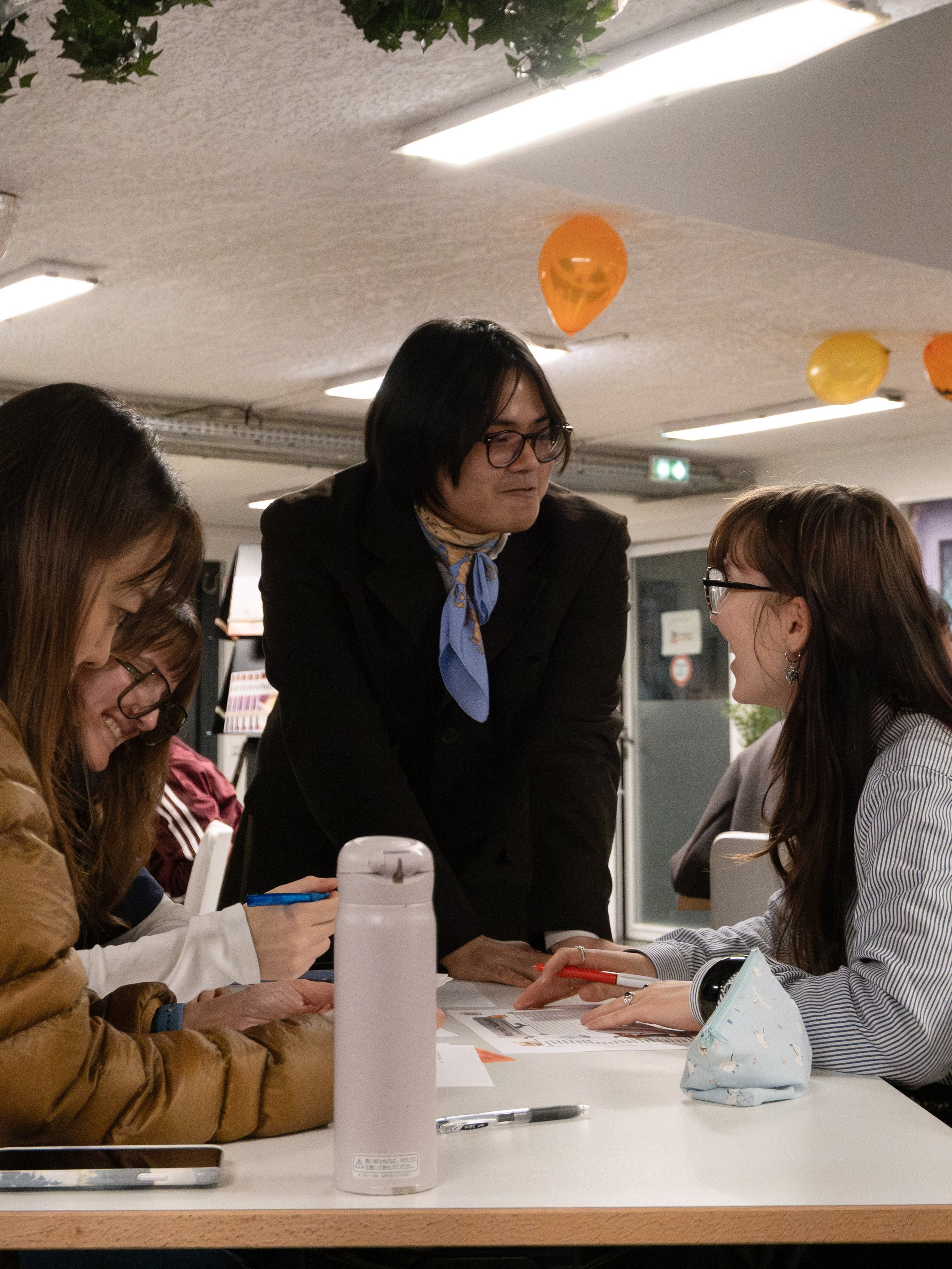 Groupe de personnes discutant autour d'une table dans une ambiance de fête, avec des décorations de Halloween en haut du plafond.