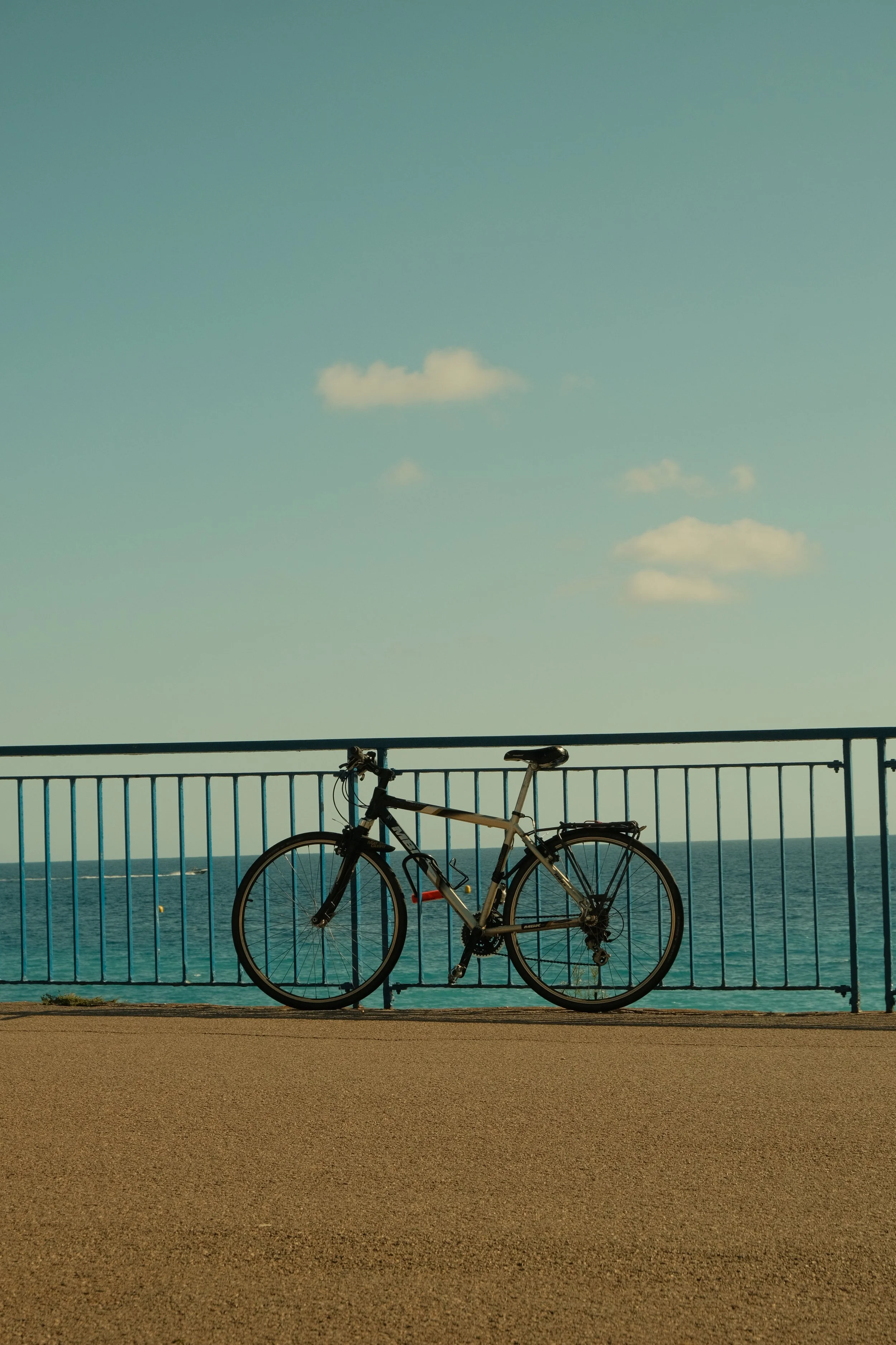 Vélo garé contre une barrière en face de la mer, avec le ciel et quelques nuages en arrière-plan.