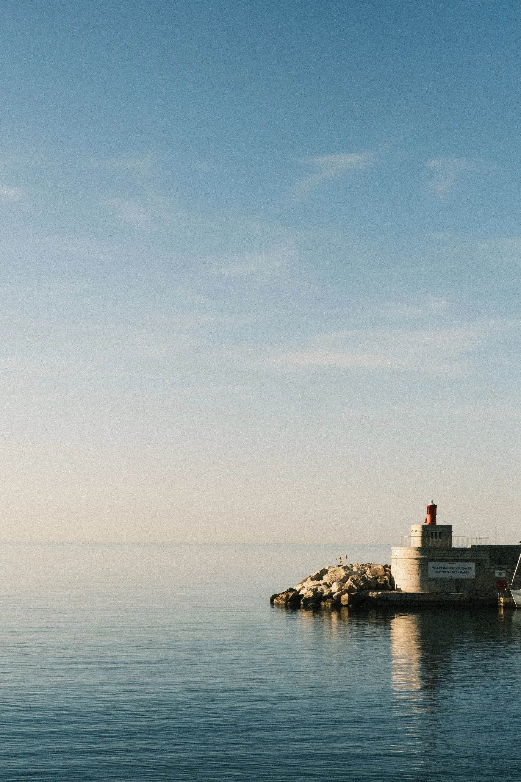 Phare sur un quai en pierre au bord de la mer avec un ciel bleu clair.