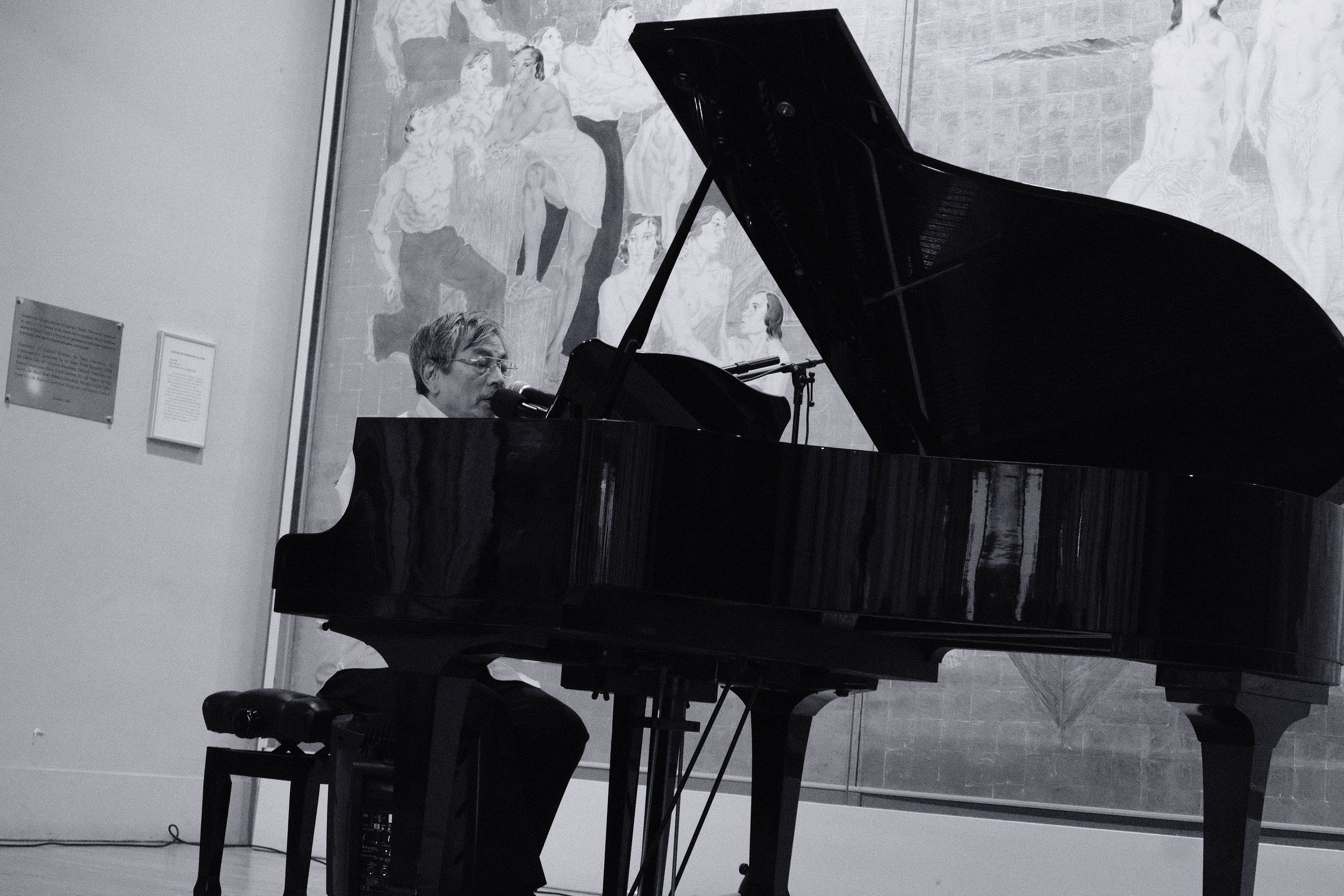 Homme jouant du piano noir à l'intérieur d'un musée, avec un tableau mural en arrière-plan.