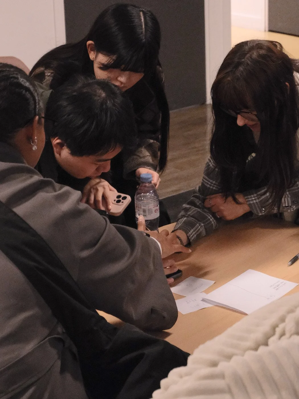 Groupe de quatre personnes rassemblées autour d'une table, concentrées sur quelque chose, avec des feuilles et un stylo.