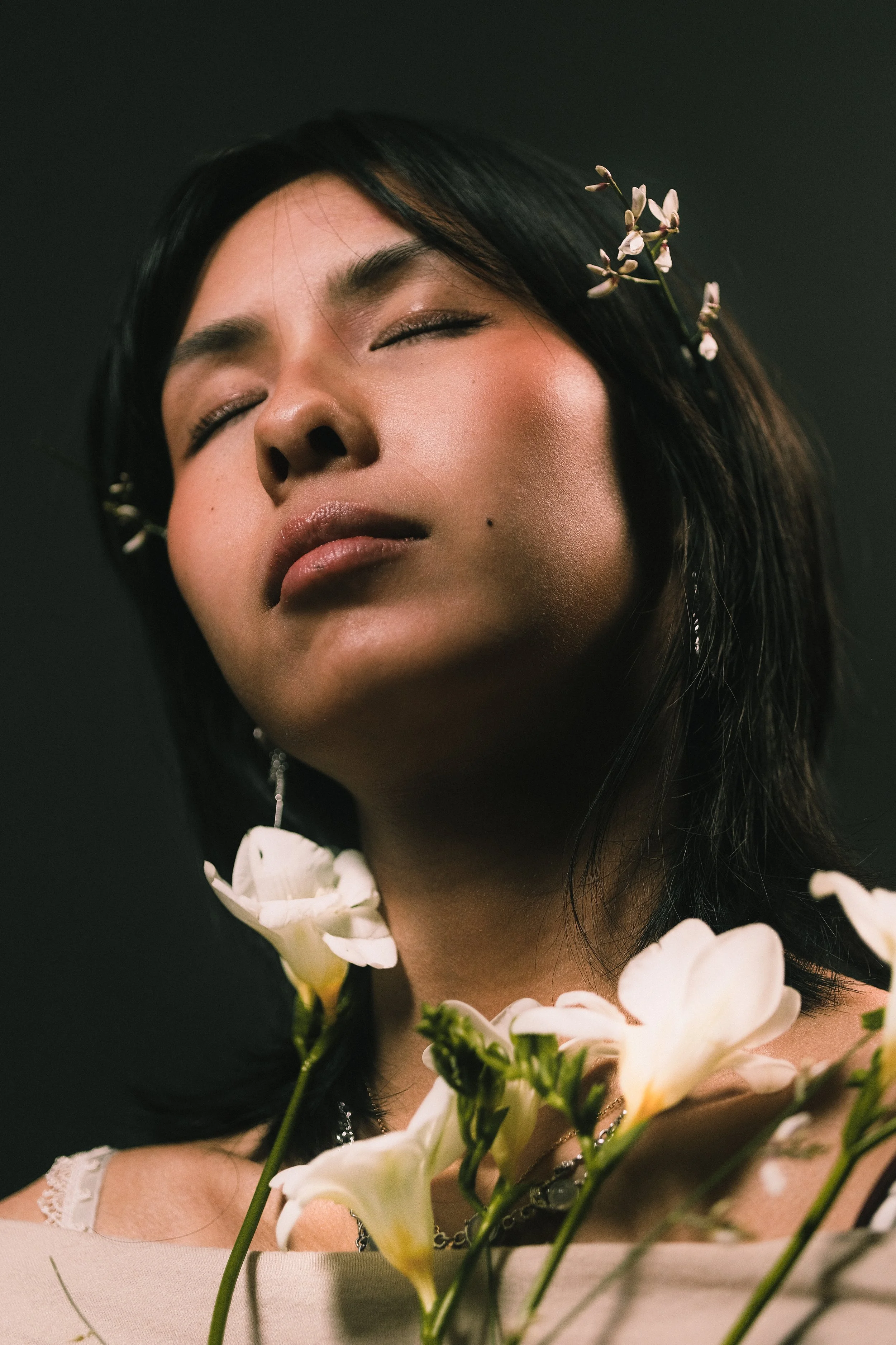 Femme avec des fleurs dans les cheveux et autour du cou, yeux fermés, expression de sérénité.