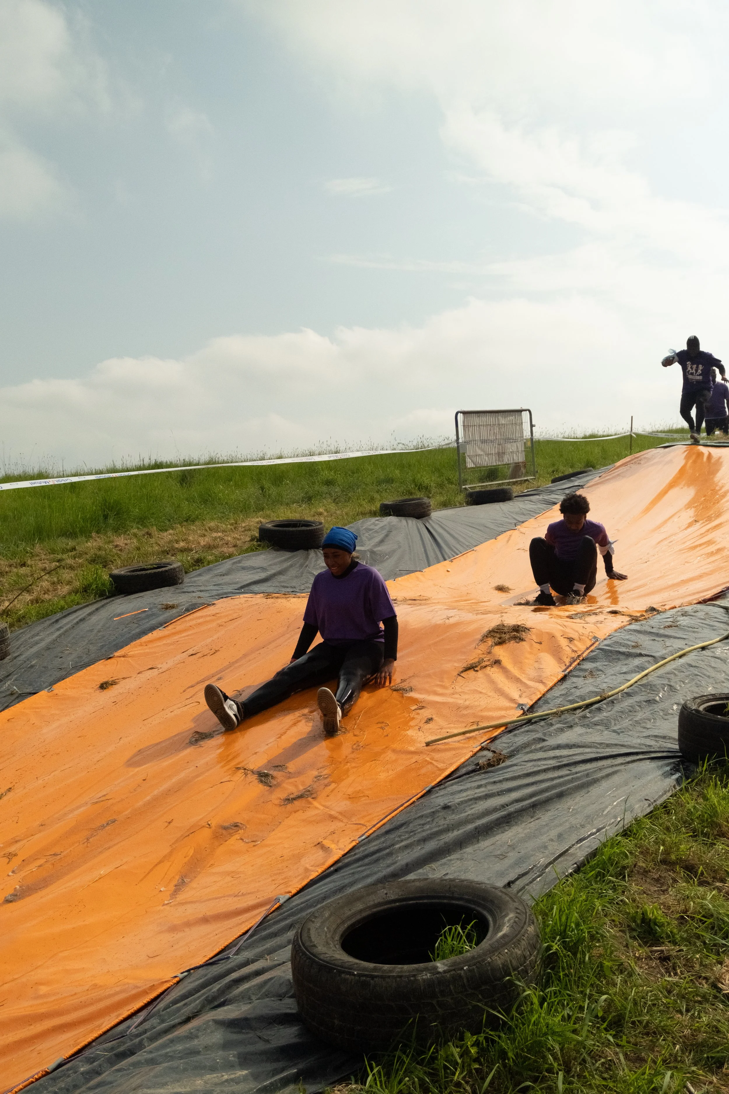 Enfants faisant la glissade sur une grande toile orange lors d'une activité en plein air.
