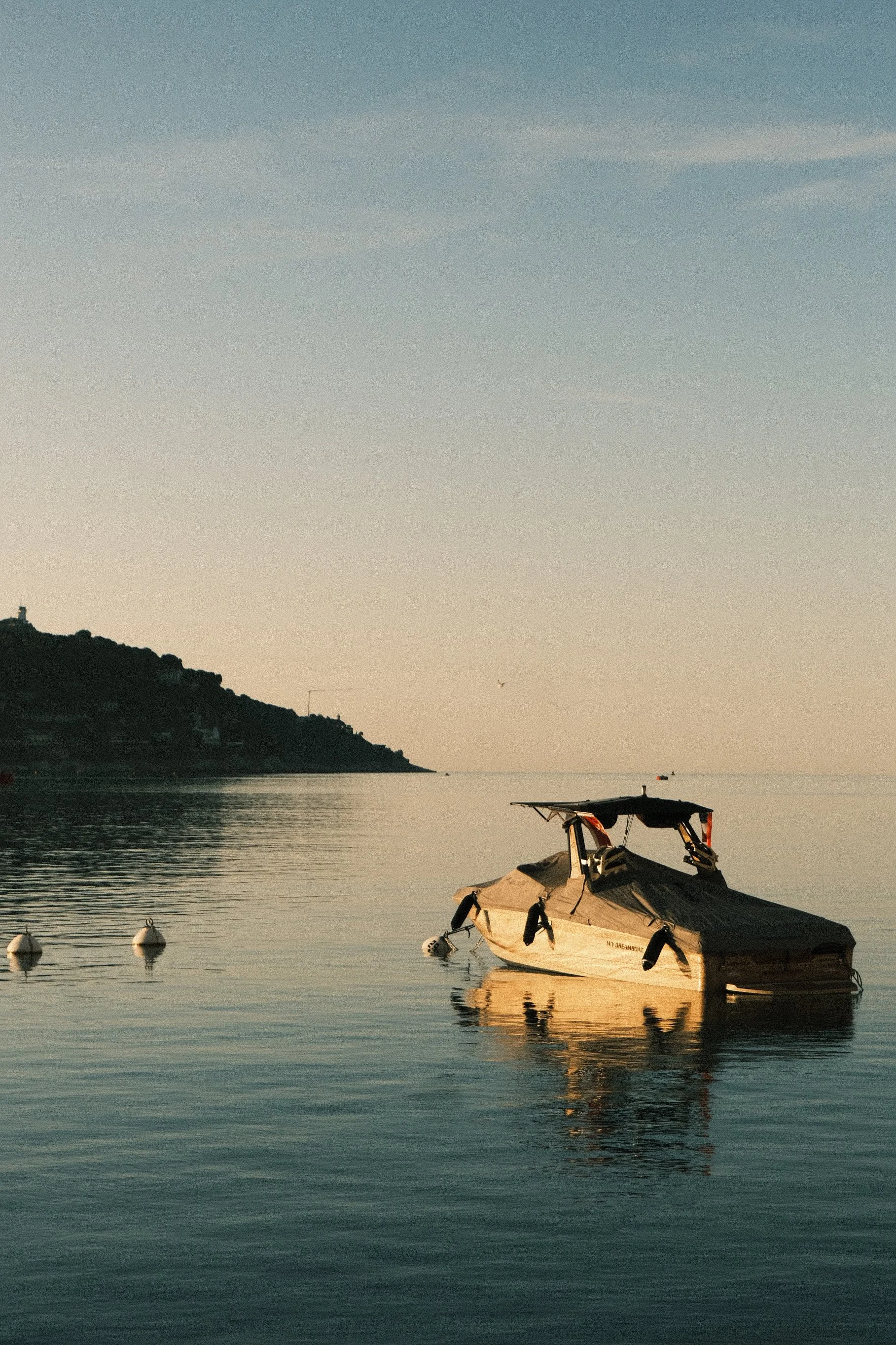 Une petite embarcation à moteur amarrée dans une mer calme, avec un paysage côtier en arrière-plan et un ciel clair.