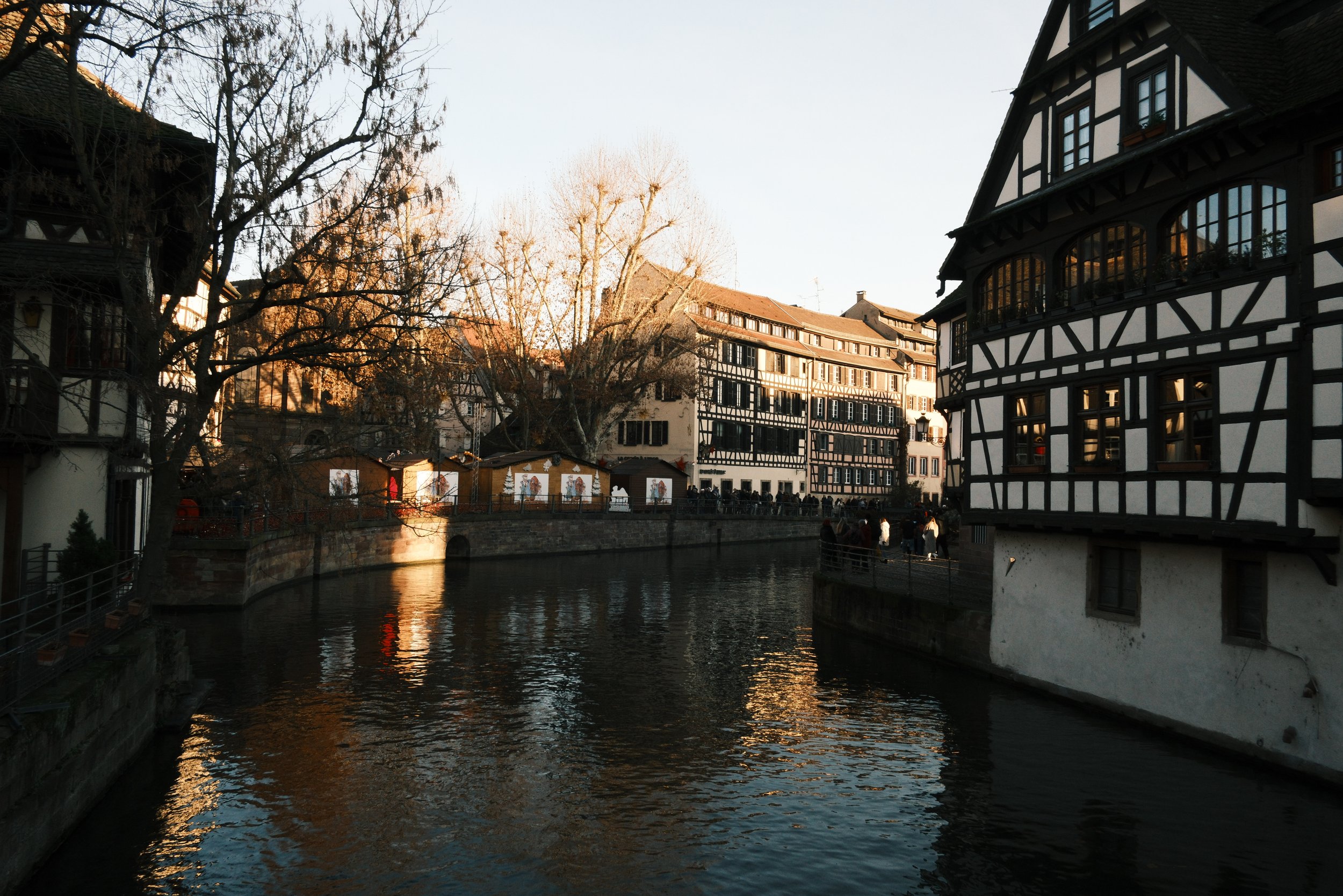Ruelle avec canal, bâtiments à colombages, arbres dénudés, au coucher du soleil.