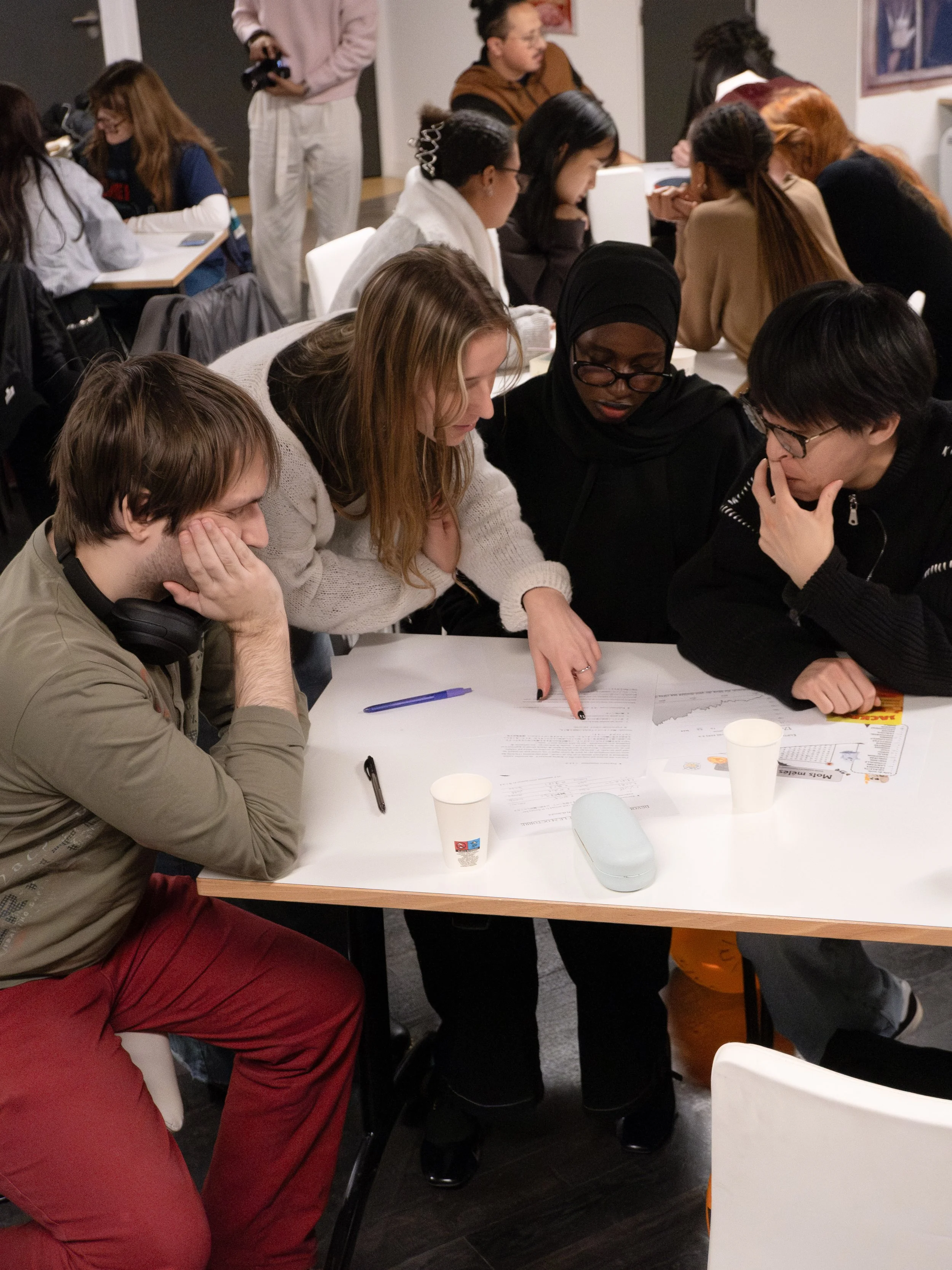 Groupe de jeunes adultes travaillant ensemble autour d'une table, en train de discuter et de consulter des documents.