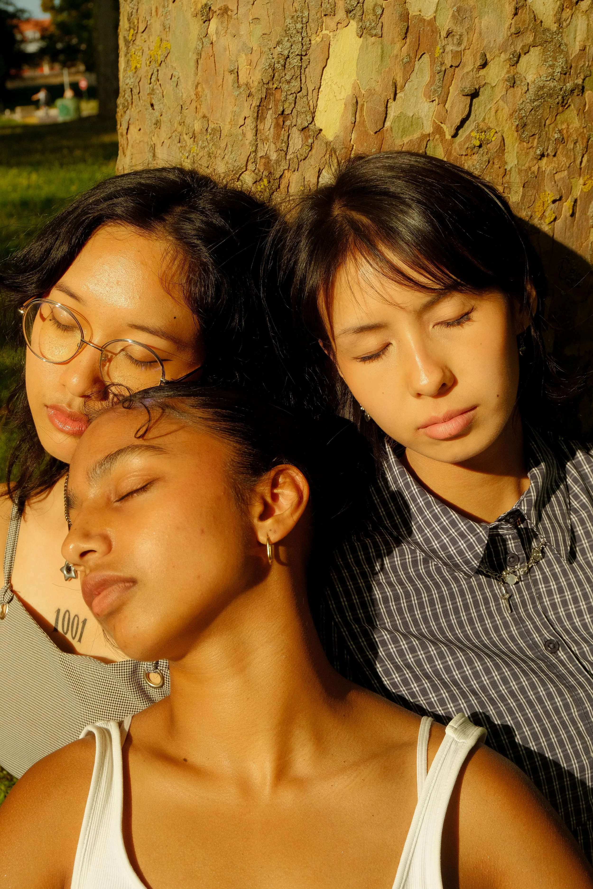 Trois jeunes femmes dorment appuyées contre un arbre dans un parc ensoleillé