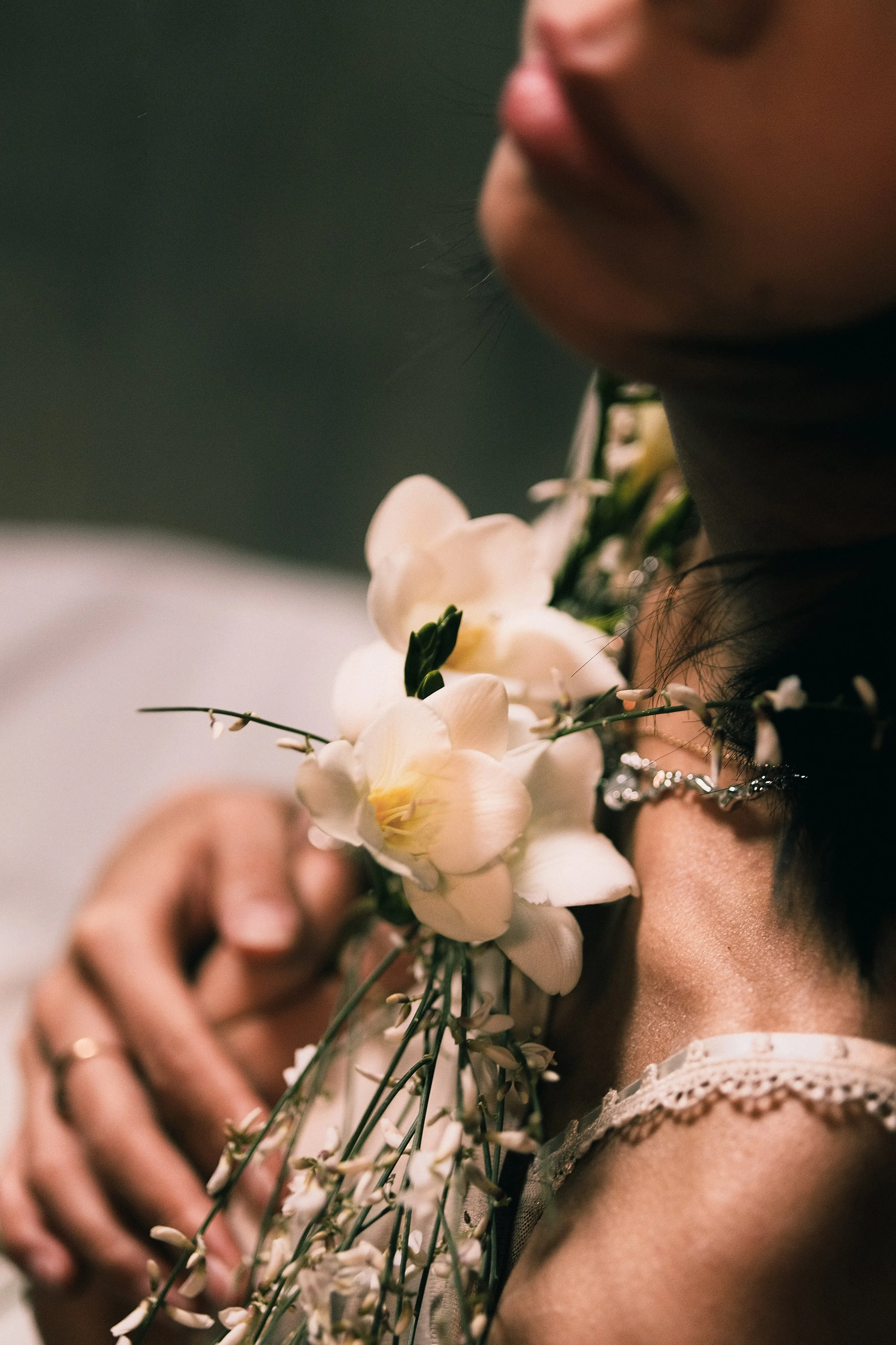 Une personne tient un bouquet de fleurs blanches, notamment des orchidées, près de son cou, avec un fond flou.