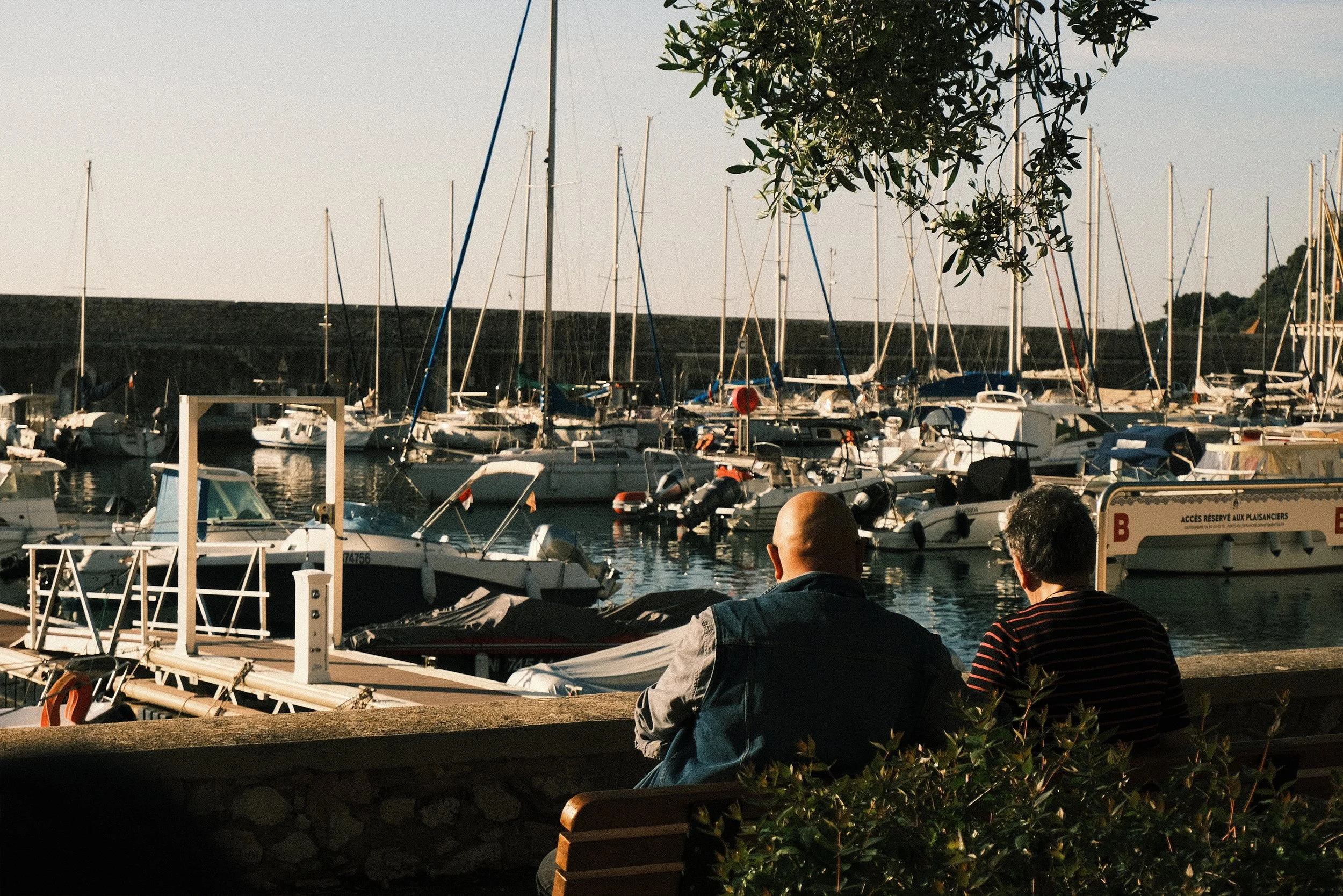 Deux hommes assis sur un banc regardant des bateaux à Marne dans un port au coucher du soleil.