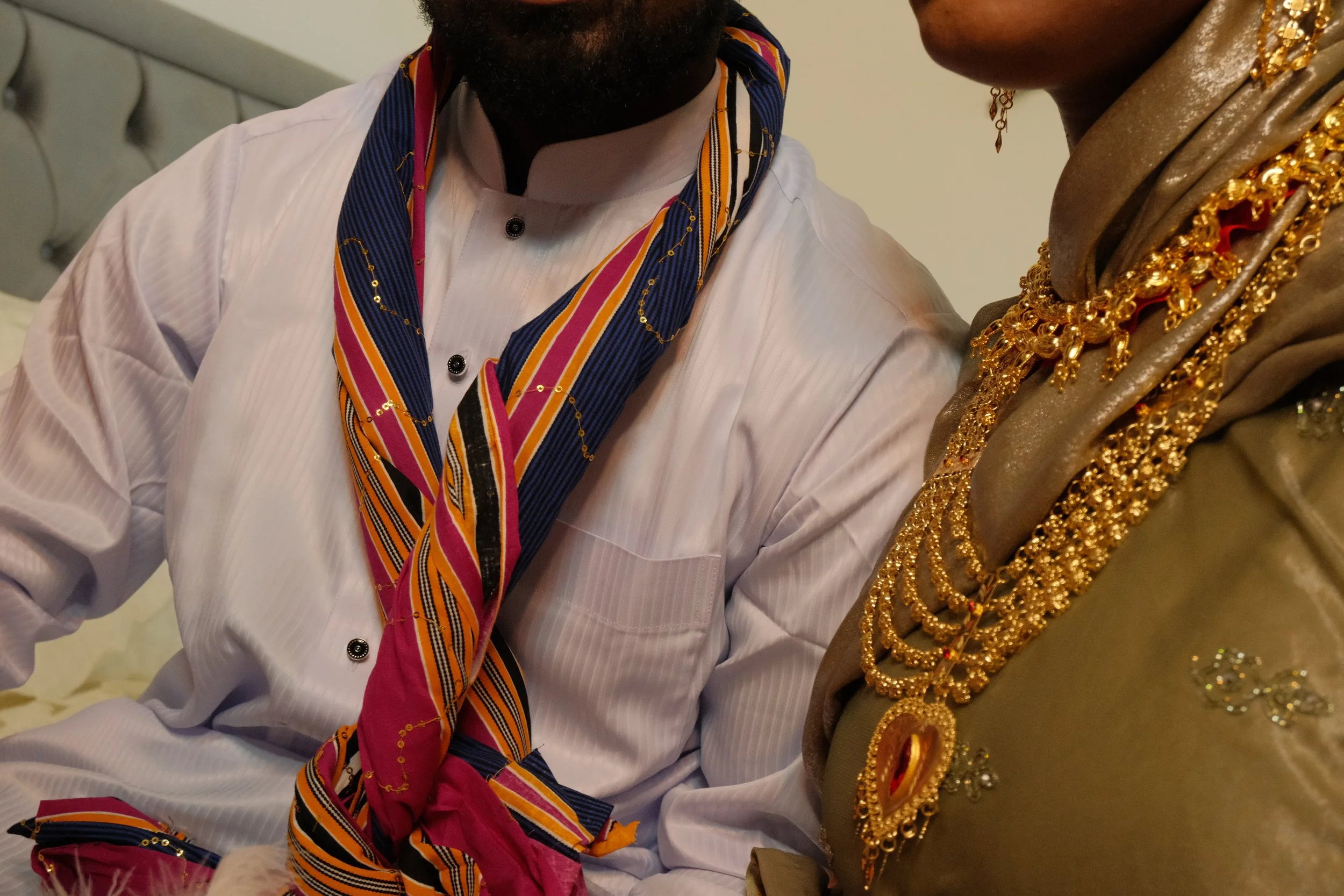 Partie de deux personnes vêtues de vêtements et bijoux dorés, avec un homme portant une chemise blanche et un autre portant plusieurs colliers en or.