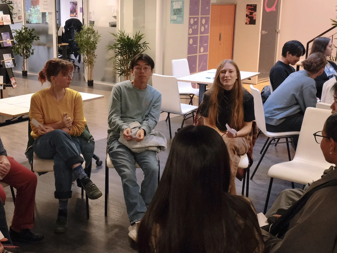Groupe de jeunes assis en cercle dans une salle, apparemment lors d'une discussion ou d'un atelier, avec une ambiance calme et studieuse.