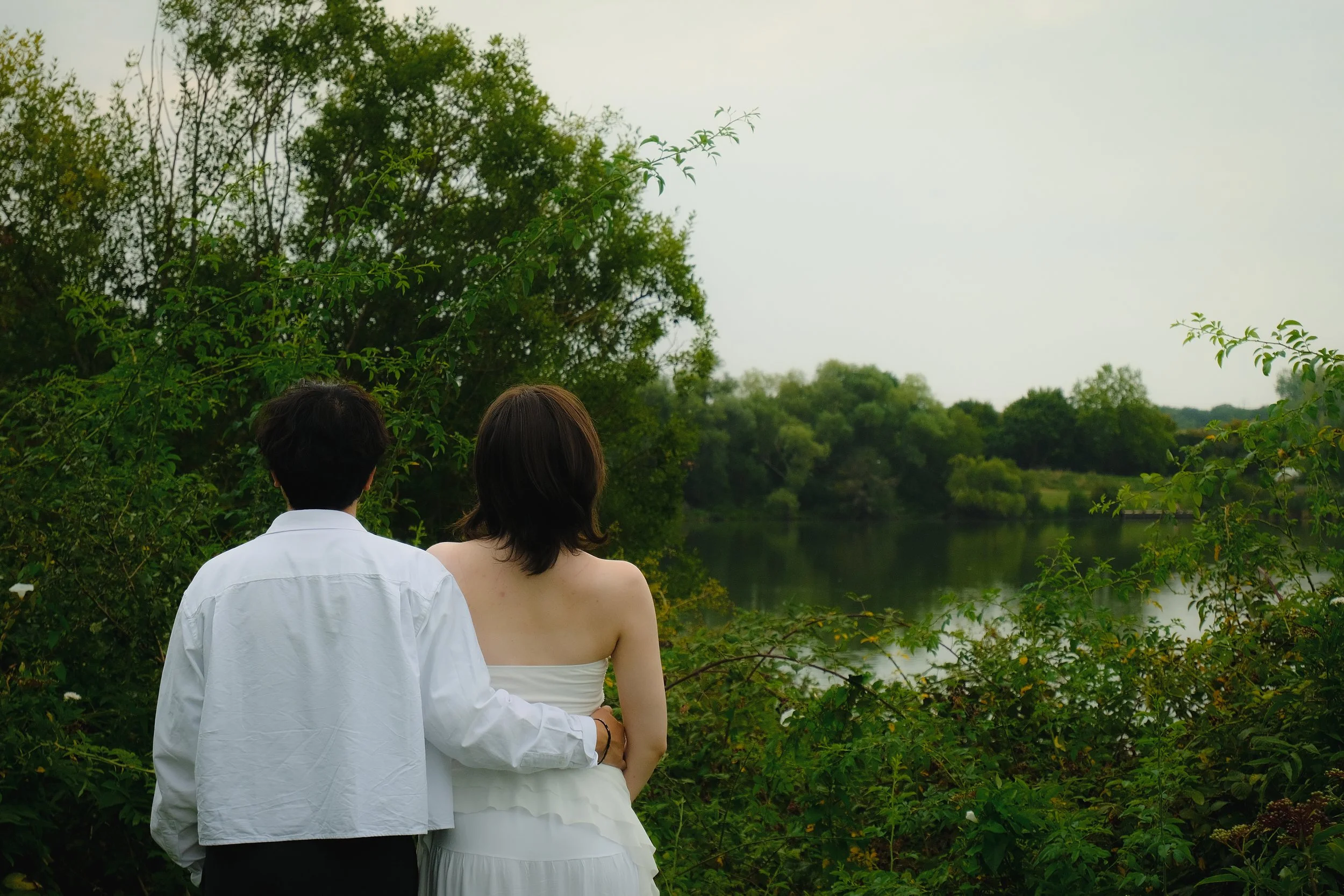 Un couple regarde une rivière entourée d'arbres, vu de dos.