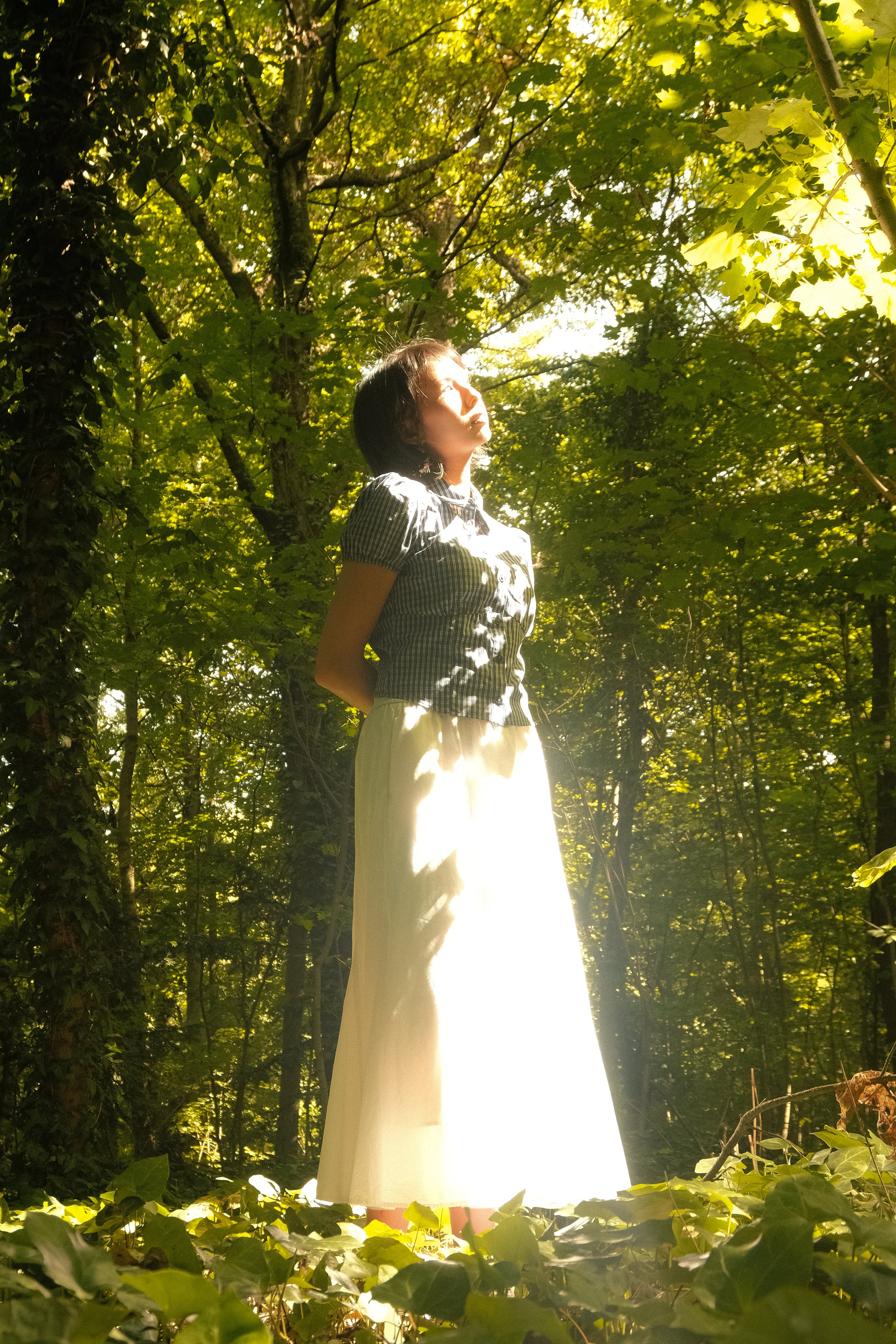 Une femme debout dans une forêt verdoyante, éclairée par un rayon de soleil.