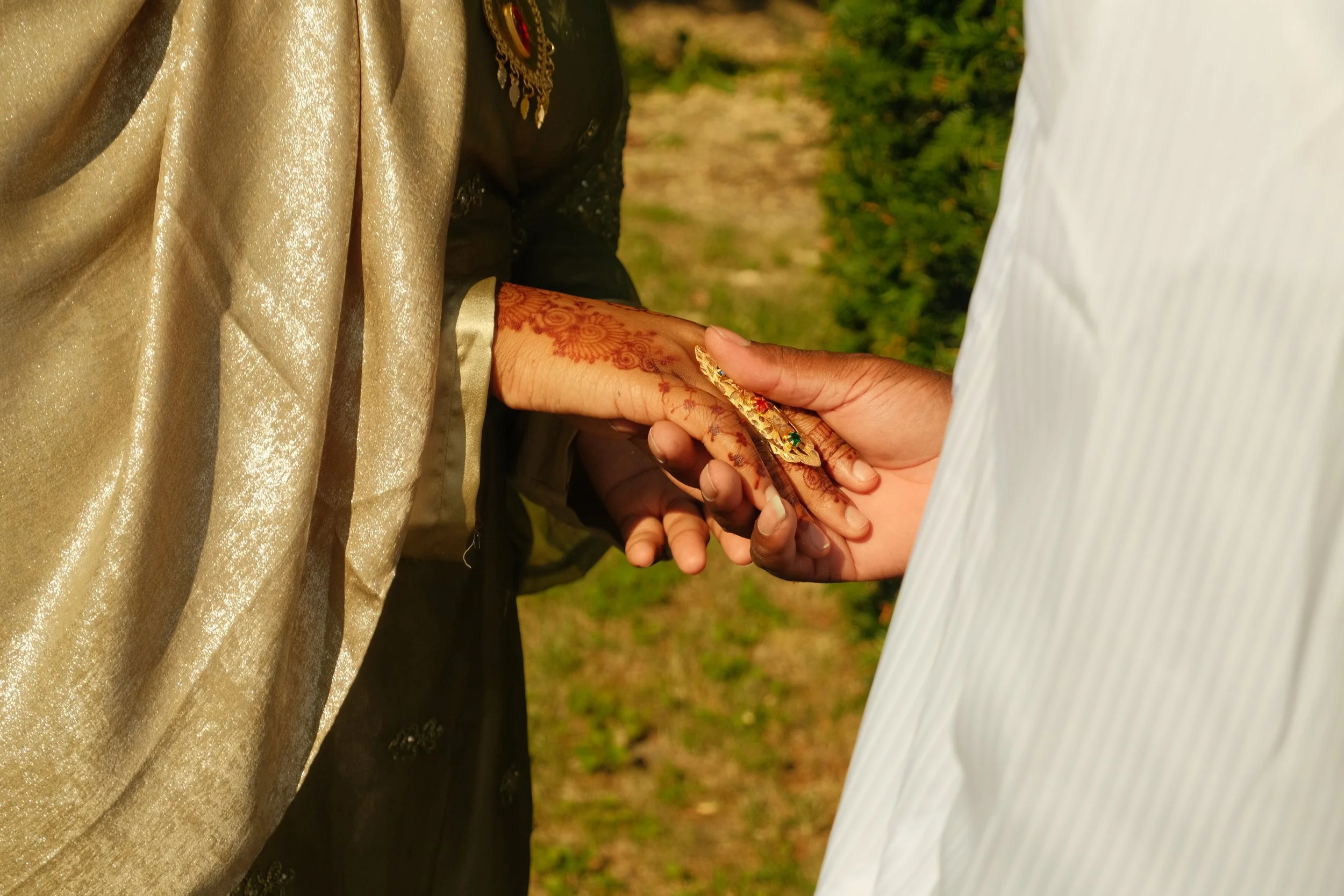 Deux personnes se tiennent la main lors d'une cérémonie de mariage, avec des mains liées, soulignant l'engagement, dans un environnement extérieur vert.