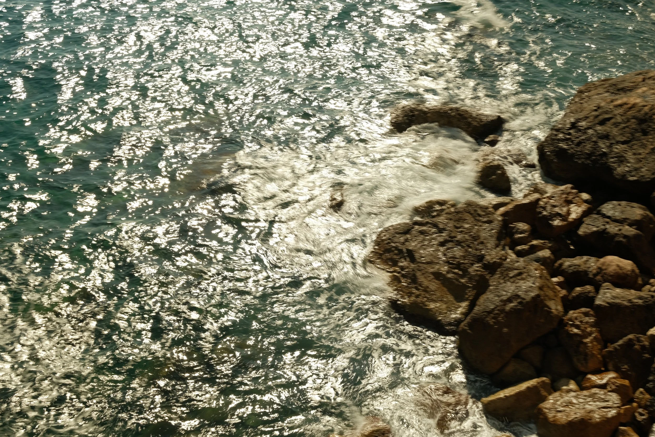 Vagues éclaboussant contre des rochers au bord de la mer avec un reflet brillant du soleil sur l'eau.
