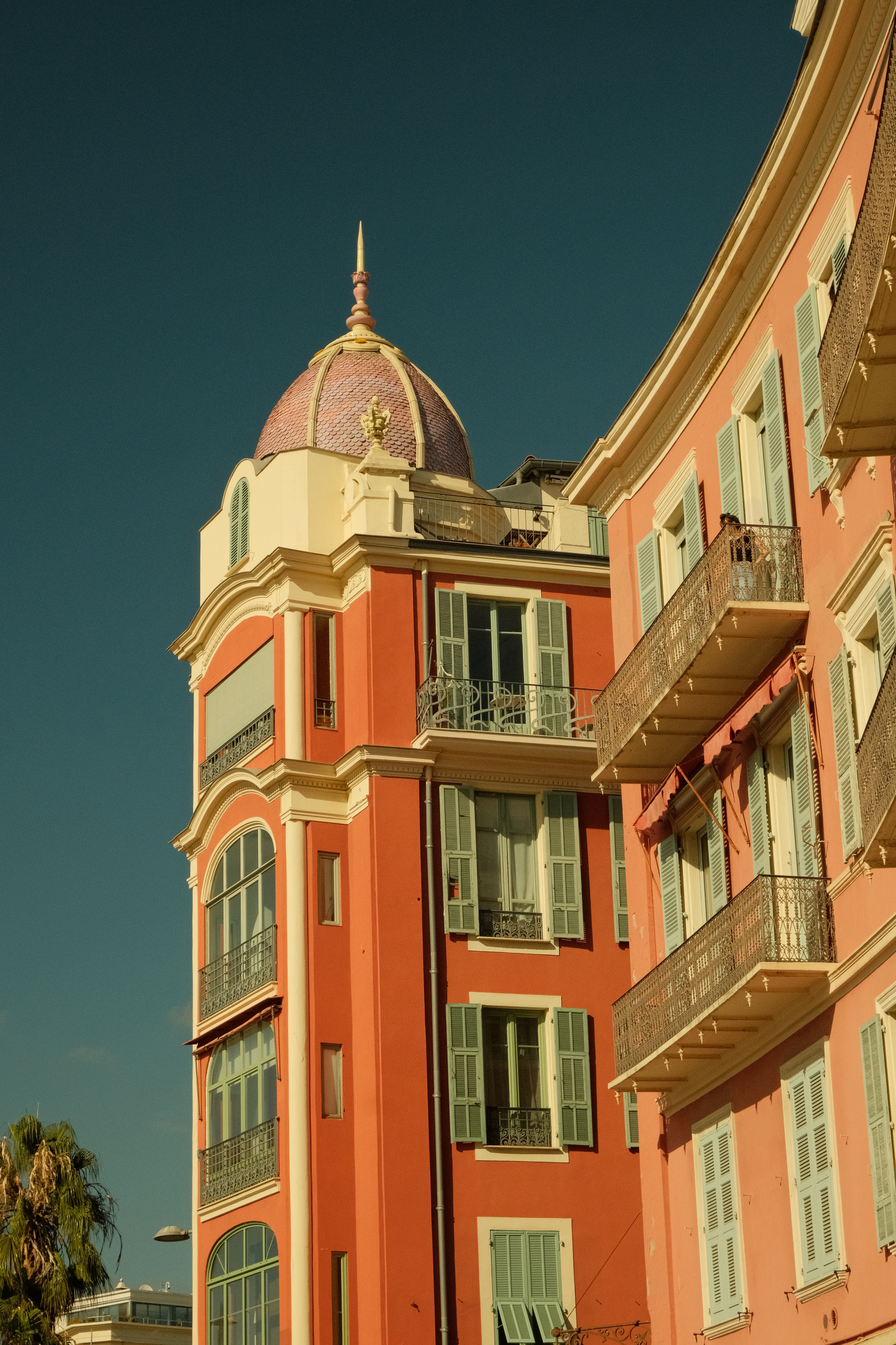 Bâtiment résidentiel coloré avec des fenêtres à volets verts et balcons en fer forgé, avec un dôme au sommet contre un ciel dégagé.