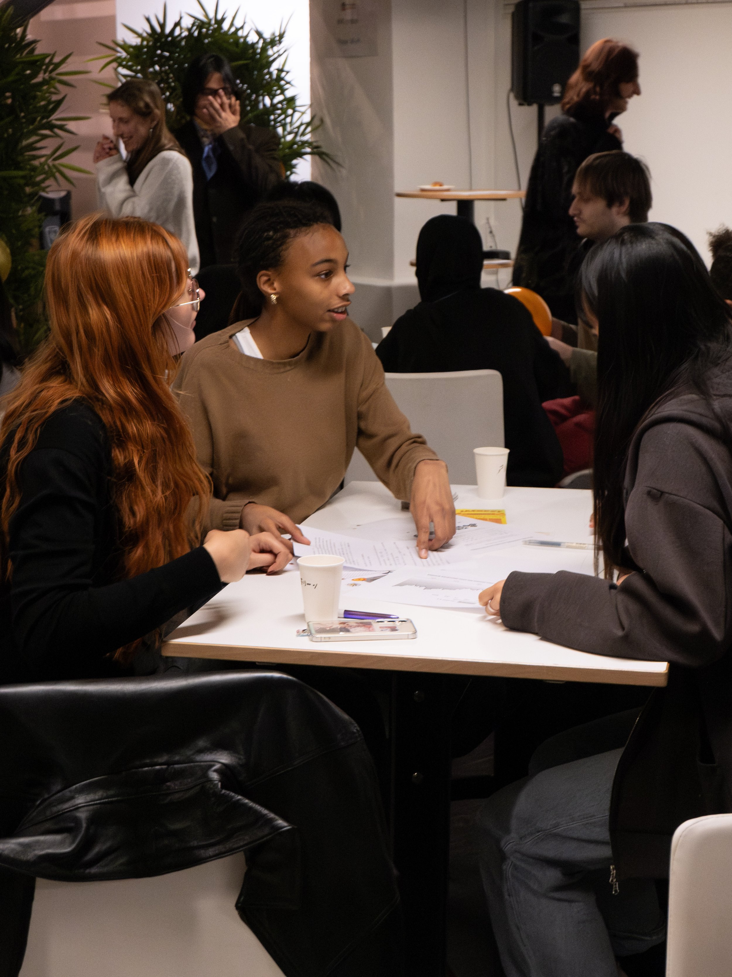 Groupe de jeunes femmes discutant autour d'une table lors d'un événement intérieur.