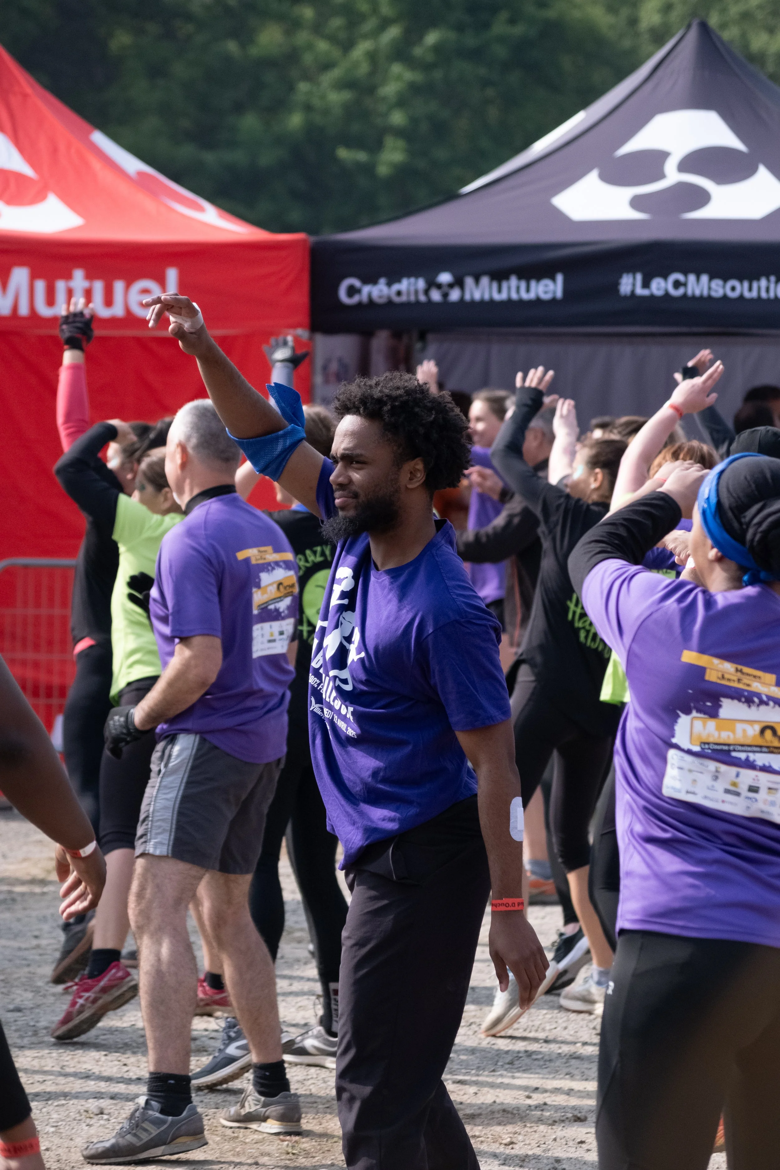 Groupe de personnes participant à une activité sportive en plein air, avec des tentes portant les logos 'Mutuel' et 'Crédit Mutuel' en arrière-plan.