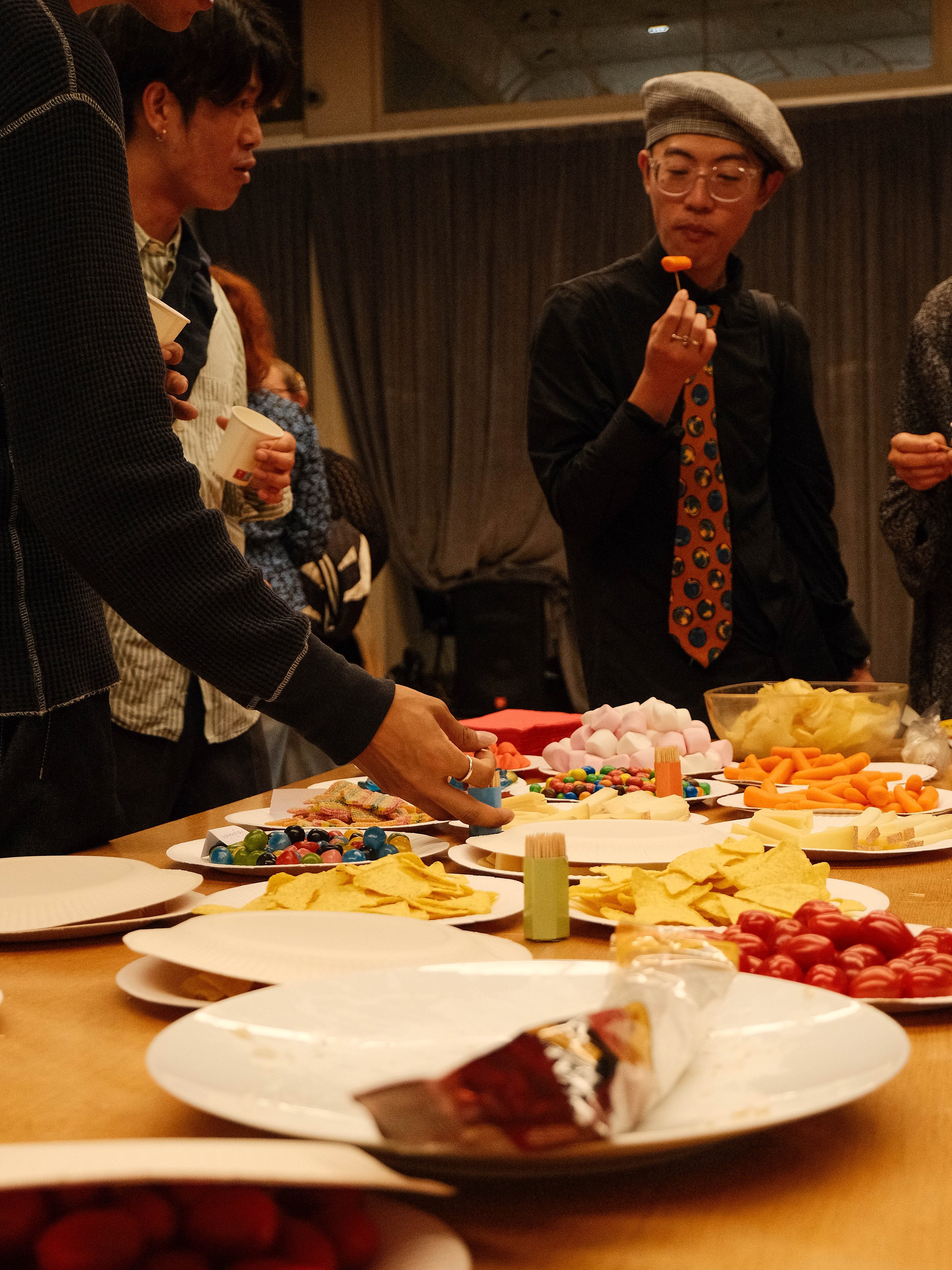 Gens autour d'une table avec des bonbons, chips, et autres snacks, lors d'une réunion ou fête, avec plusieurs personnes