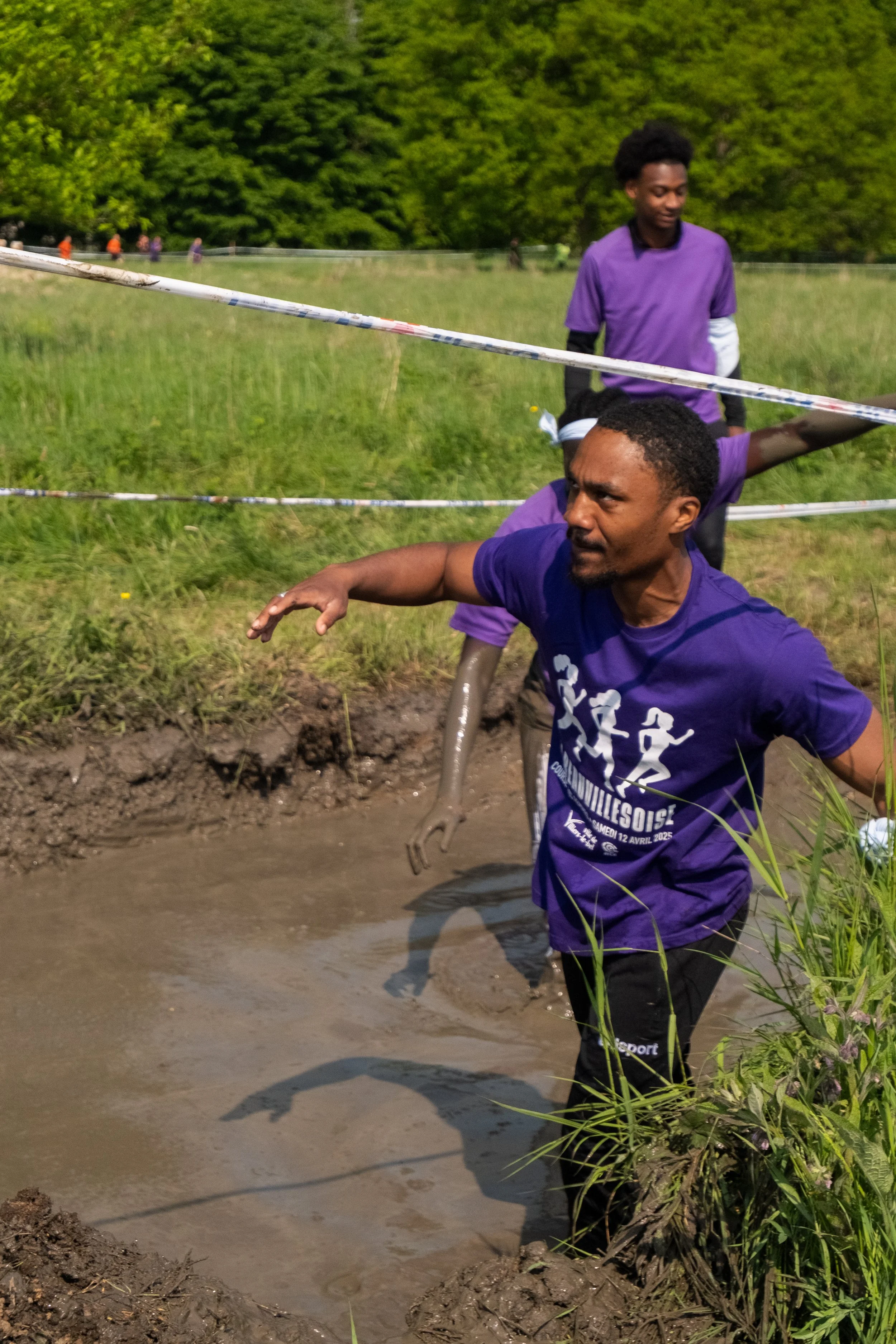 Deux hommes portant des vêtements violets traversent un trou d'eau, un d'eux est en marche dans l'eau boueuse, un autre le suit derrière.