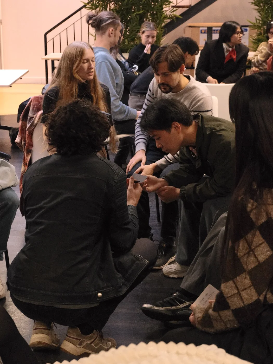 Groupe de jeunes adultes assis et discutant lors d'une réunion ou d'un atelier. Certains regardent leur téléphone, d'autres échangent entre eux.
