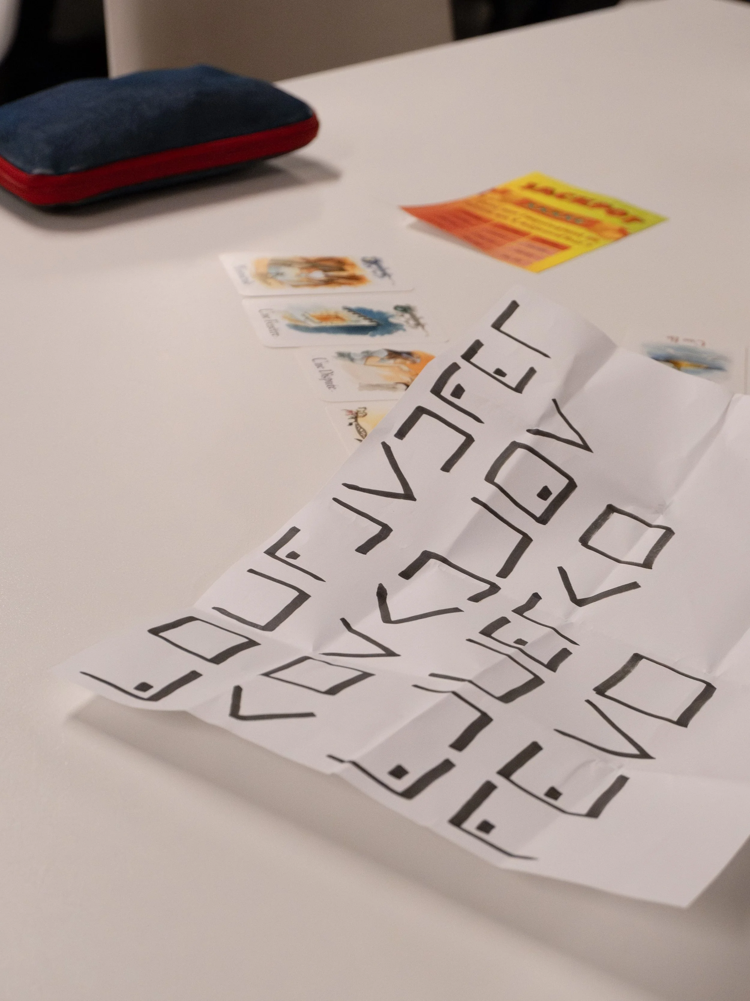 Une feuille de papier avec des lettres en style stylisé, deux cartes avec des images et des mots, un paquet de cartes en arrière-plan, un flyer coloré.