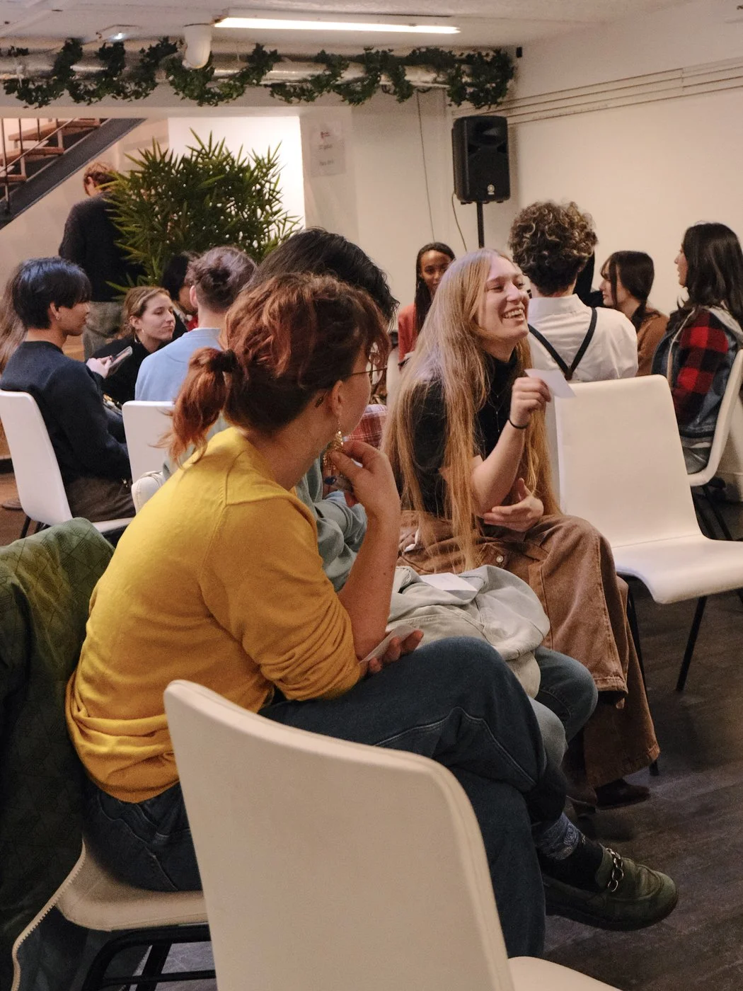 Groupe de jeunes assis et discutant dans une salle, ambiance chaleureuse et conviviale.