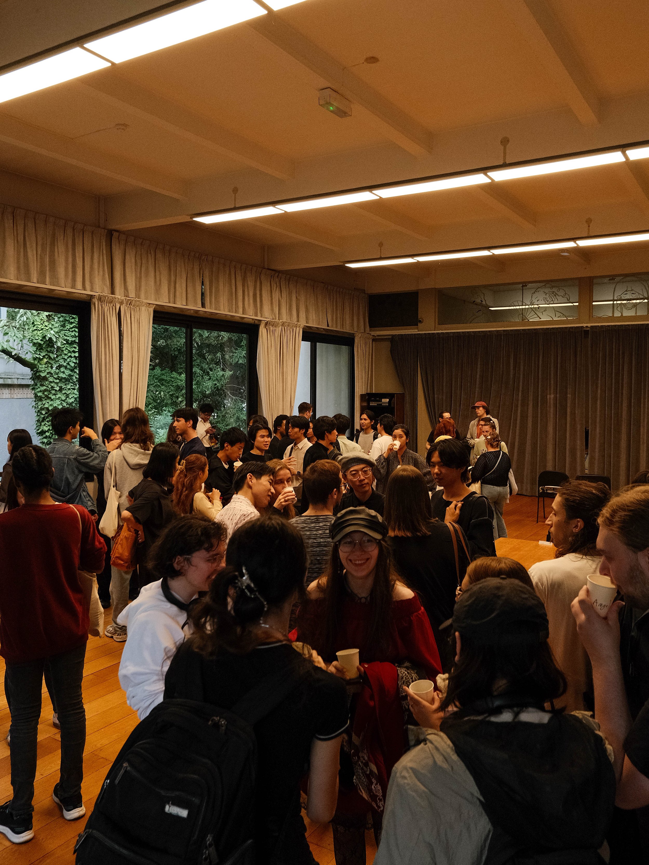 Un groupe de personnes dans une salle en train de discuter et de socialiser, avec des fenêtres grandes laissant entrer la lumière naturelle.