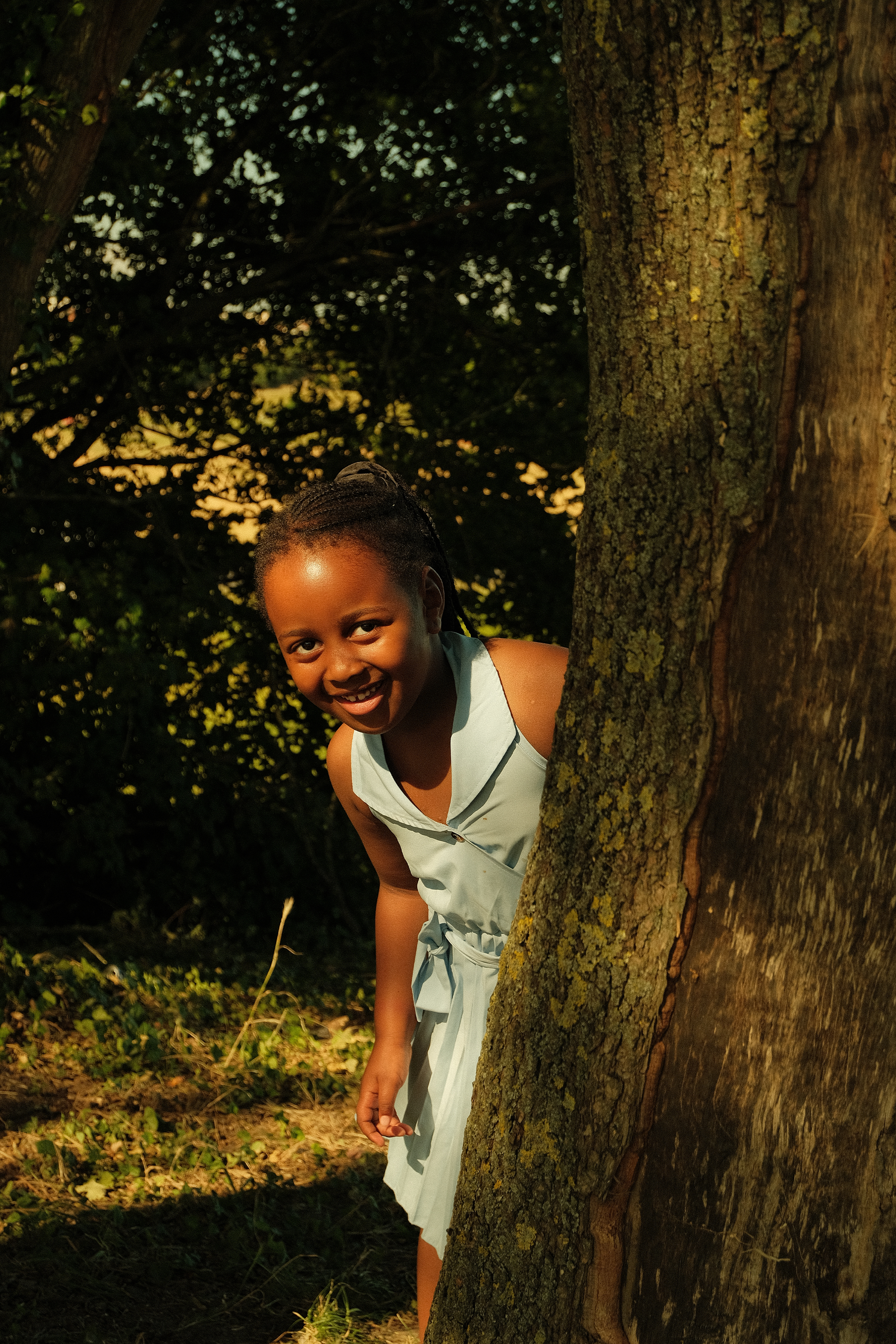 Une jeune fille souriante qui regarde par derrière un arbre dans une forêt.
