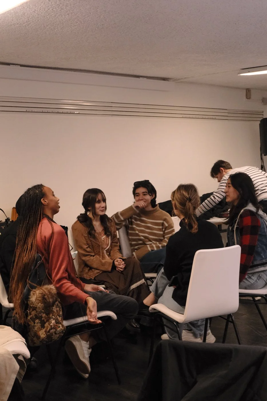Groupe de jeunes adultes en discussion dans une salle intérieure, assis en cercle.