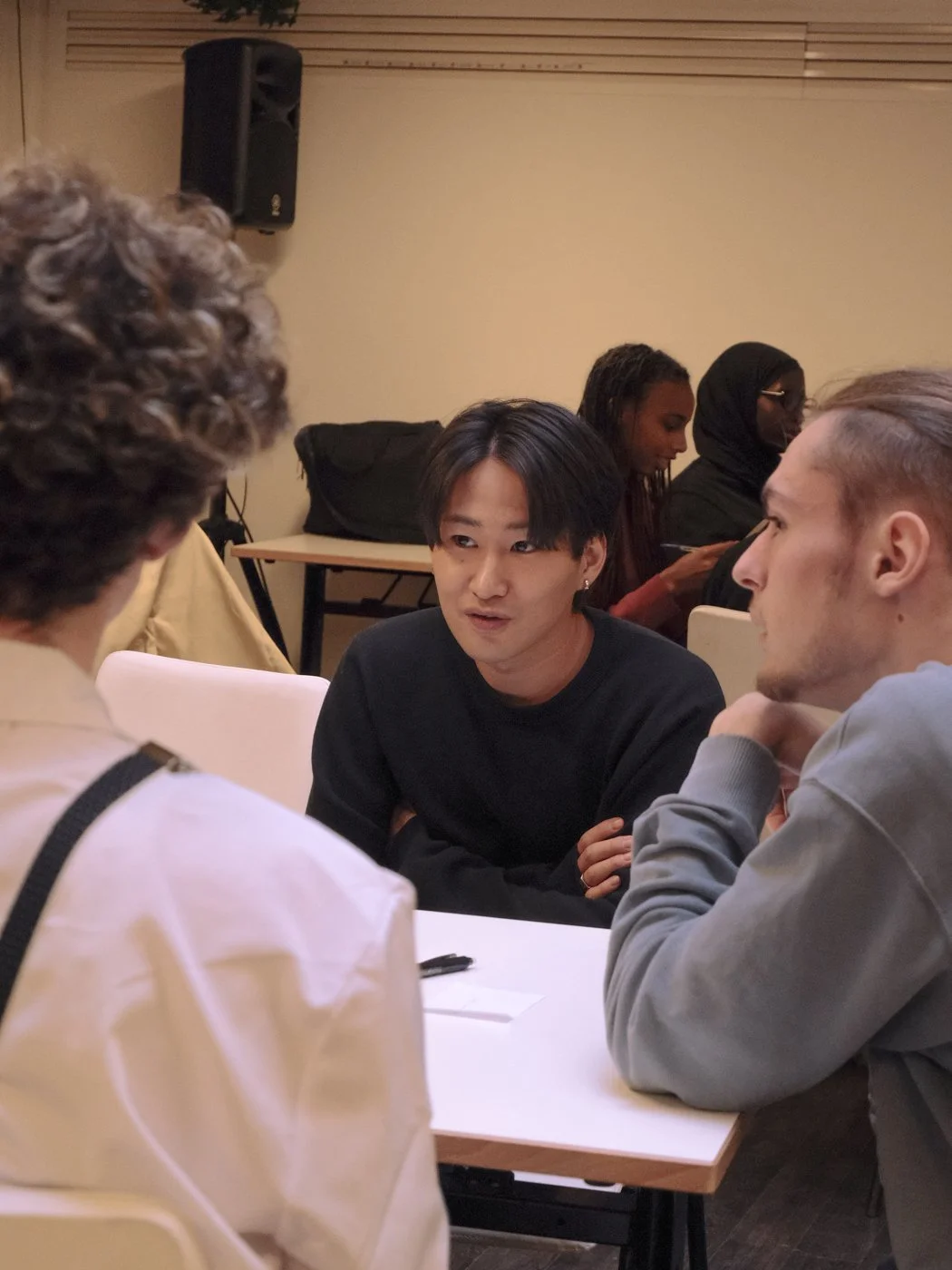 Groupe de quatre personnes discutant autour d'une table, en conversation dans une salle intérieure.