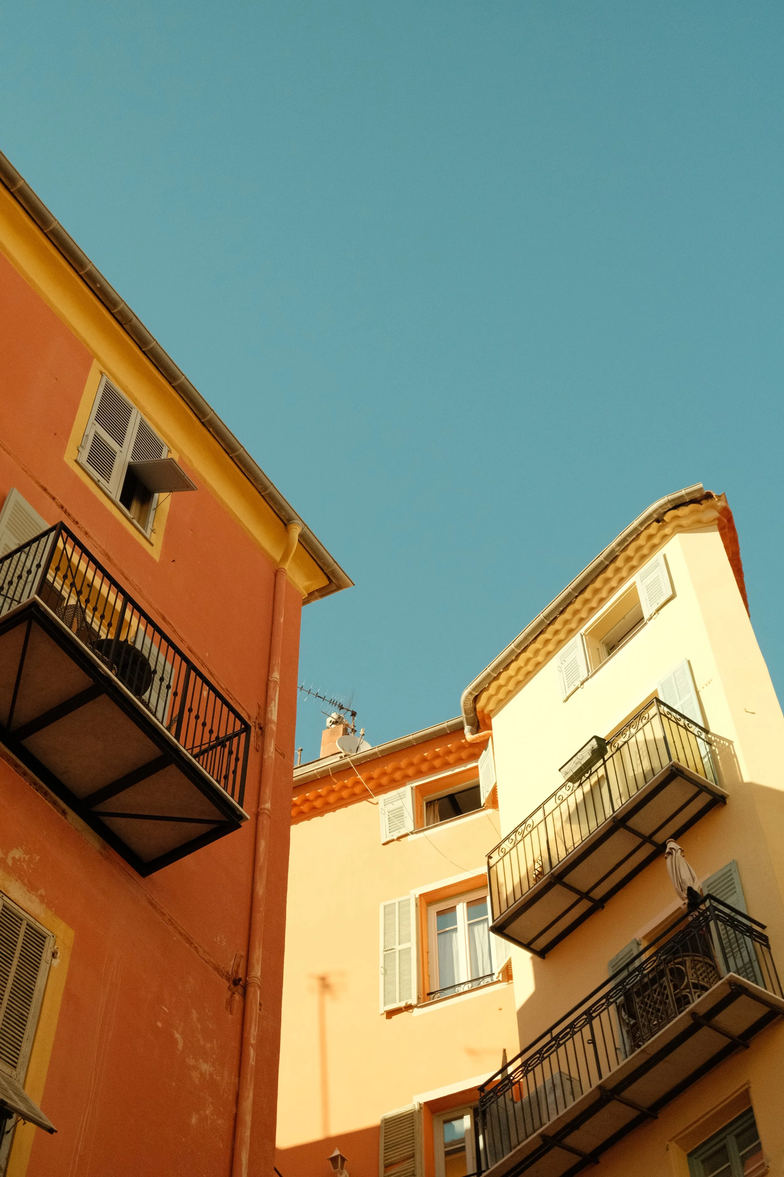Vue de côté de bâtiments colorés avec des balcons en métal, fenêtres avec volets et ciel bleu clair.