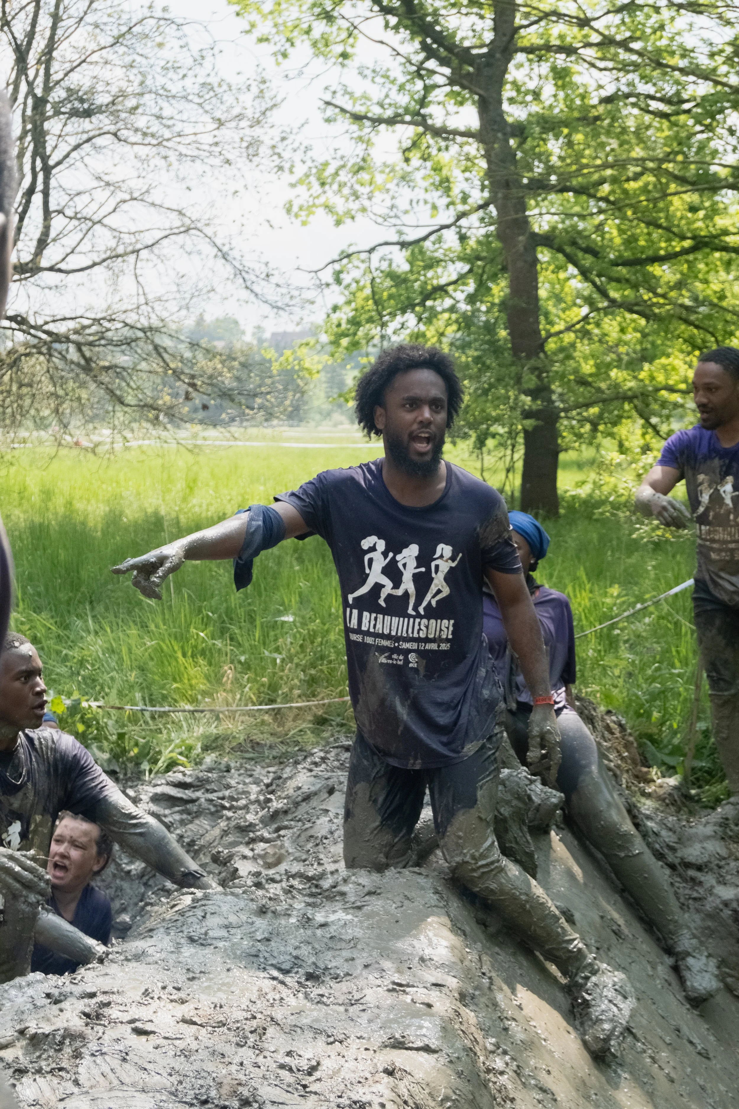 Groupe de personnes participant à une course dans la boue dans un espace vert avec des arbres.