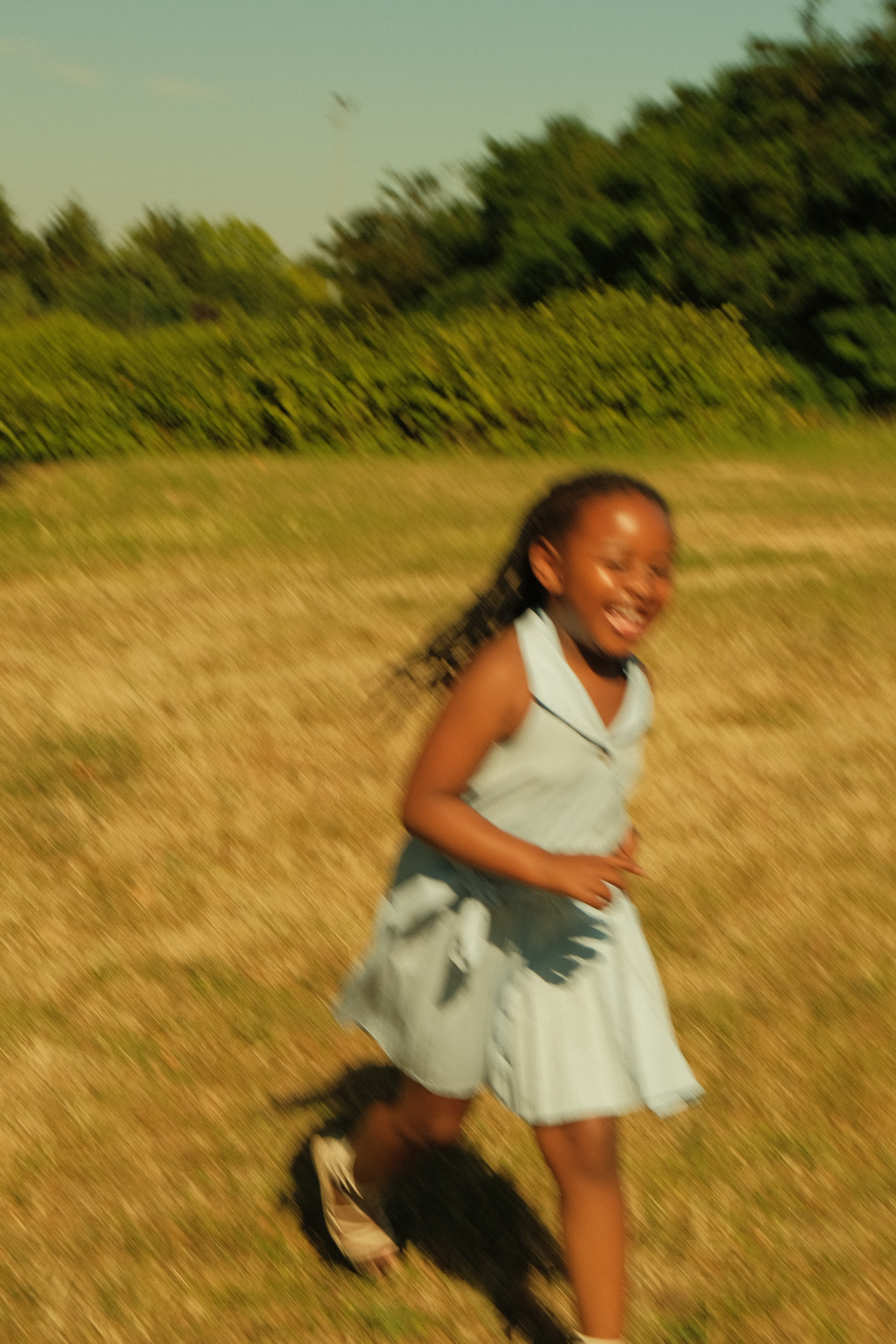 Une jeune fille souriante qui court dans un champ, portant un uniforme scolaire, avec des arbres en arrière-plan.