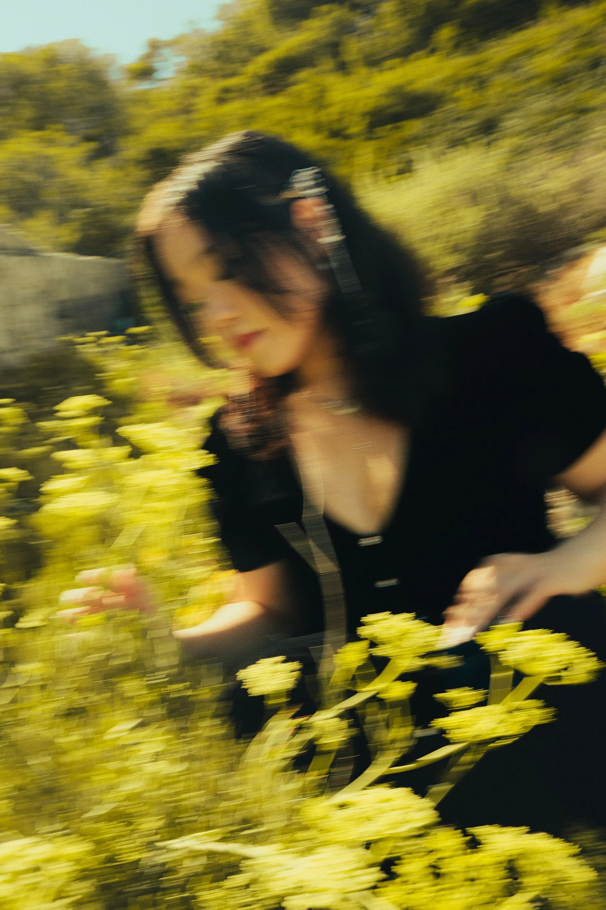 Femme floue portant un bandeau noir dans un champ de fleurs jaunes, sous la lumière du soleil, en plein air.
